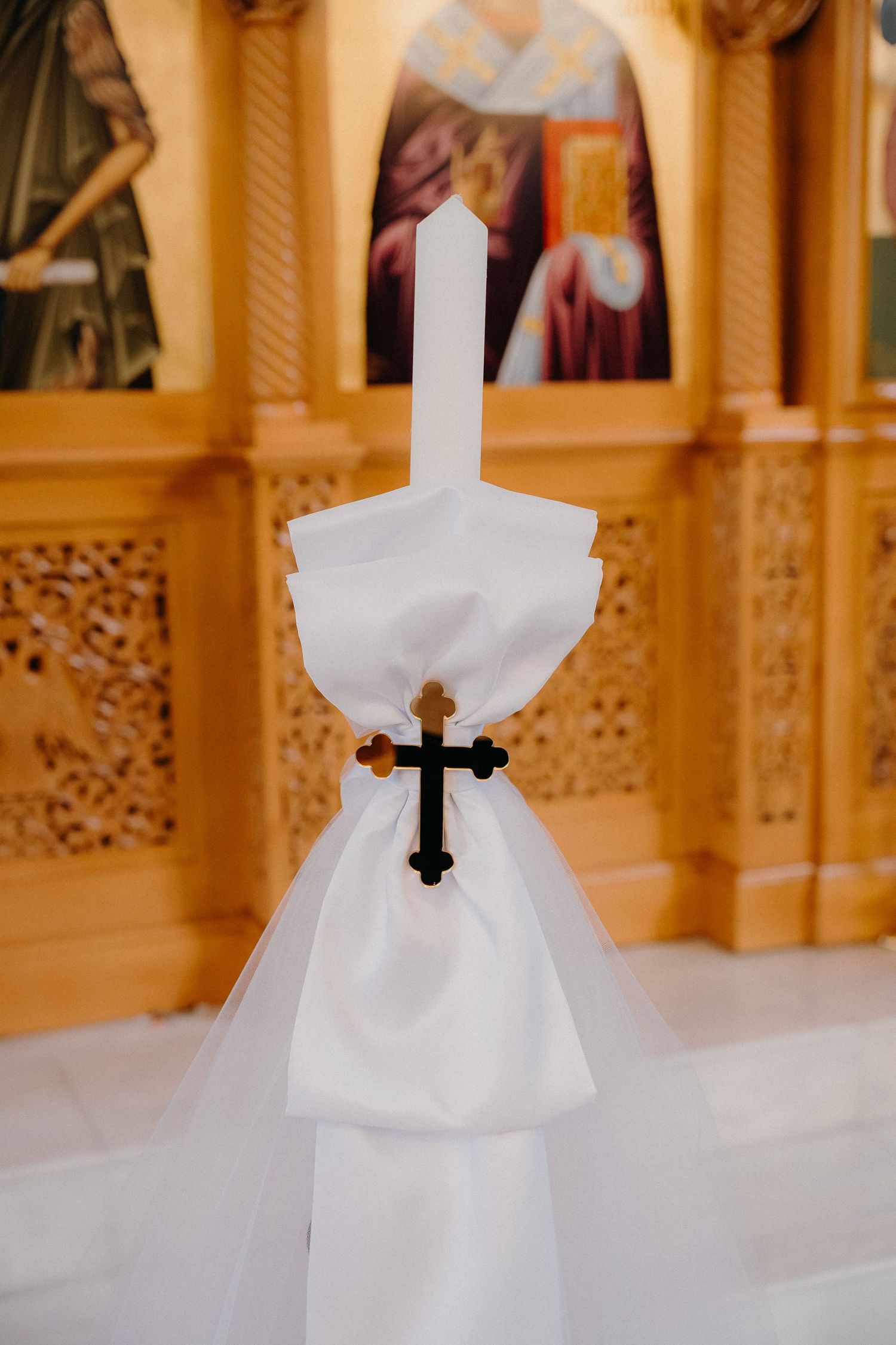 White paper napkin folded into a nun shape with black cross detail sits on golden ornate railing in church setting.