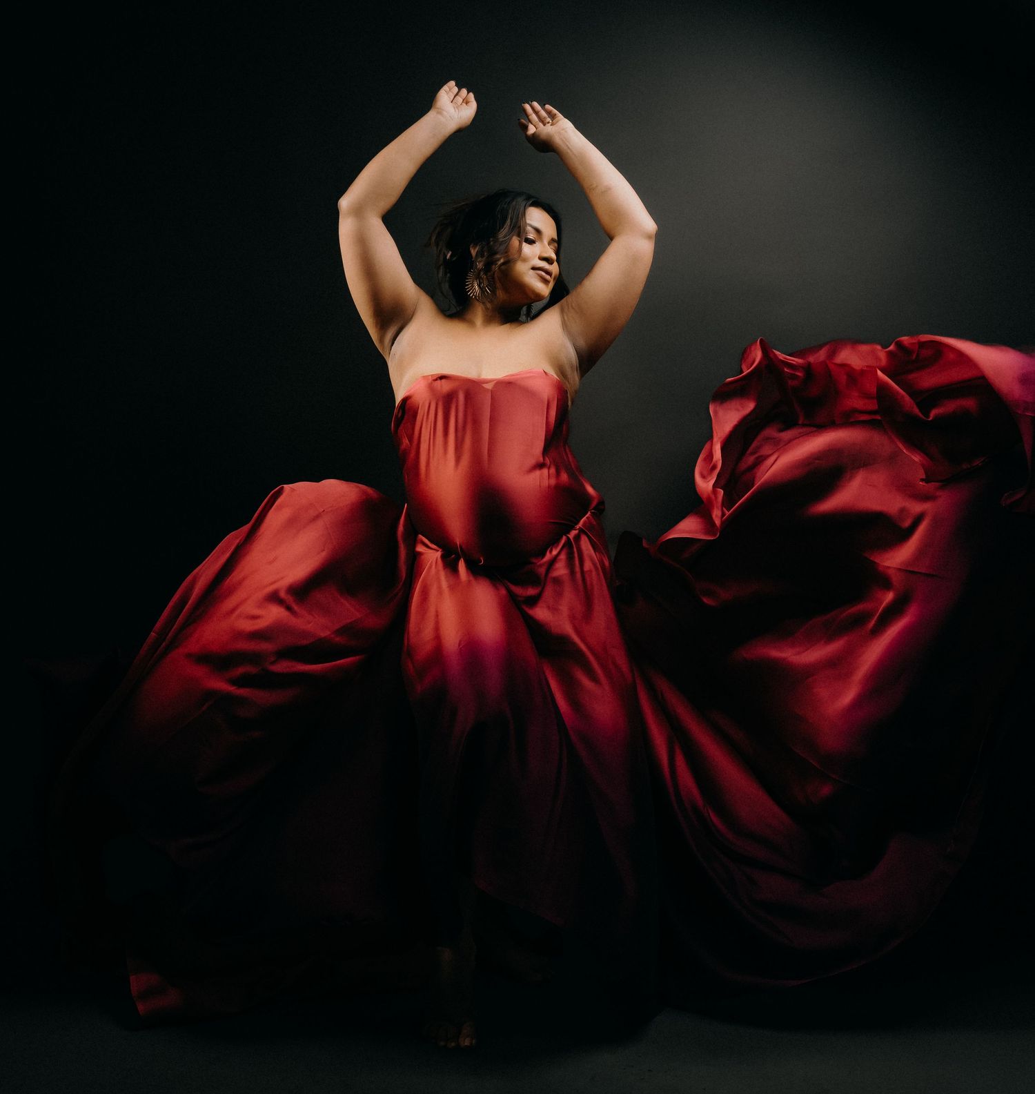 A dancer in a flowing red gown strikes a dramatic pose against a dark background as the fabric billows around them.