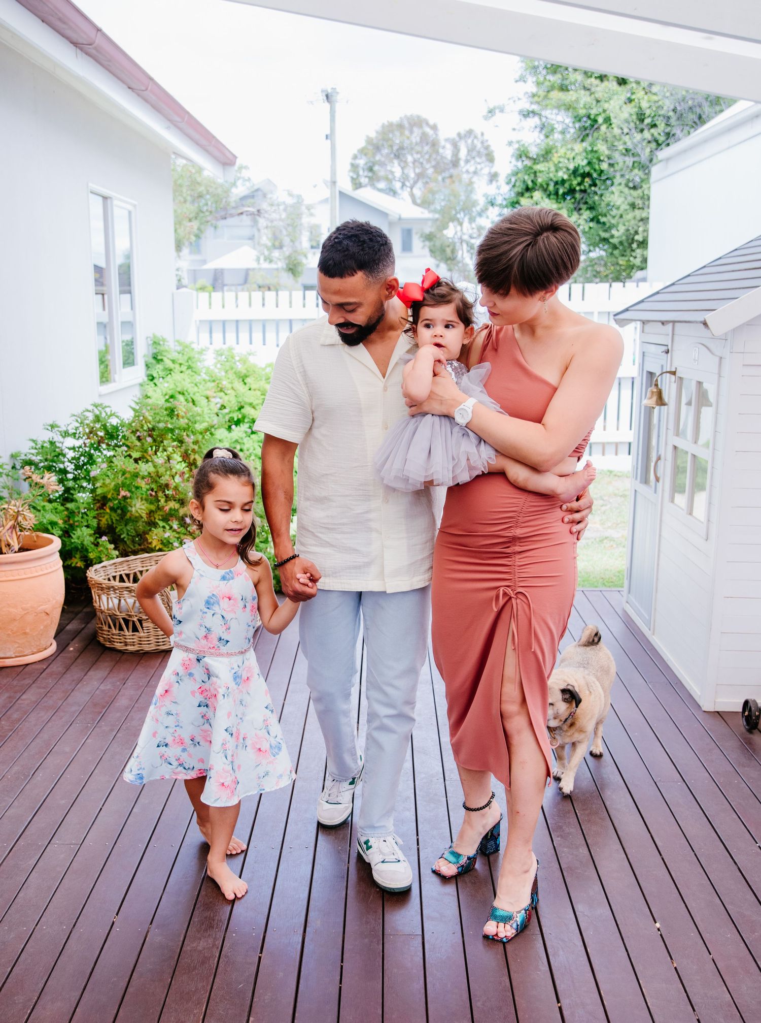 A family stands together on a wooden deck with a small dog while wearing coordinated summer outfits.