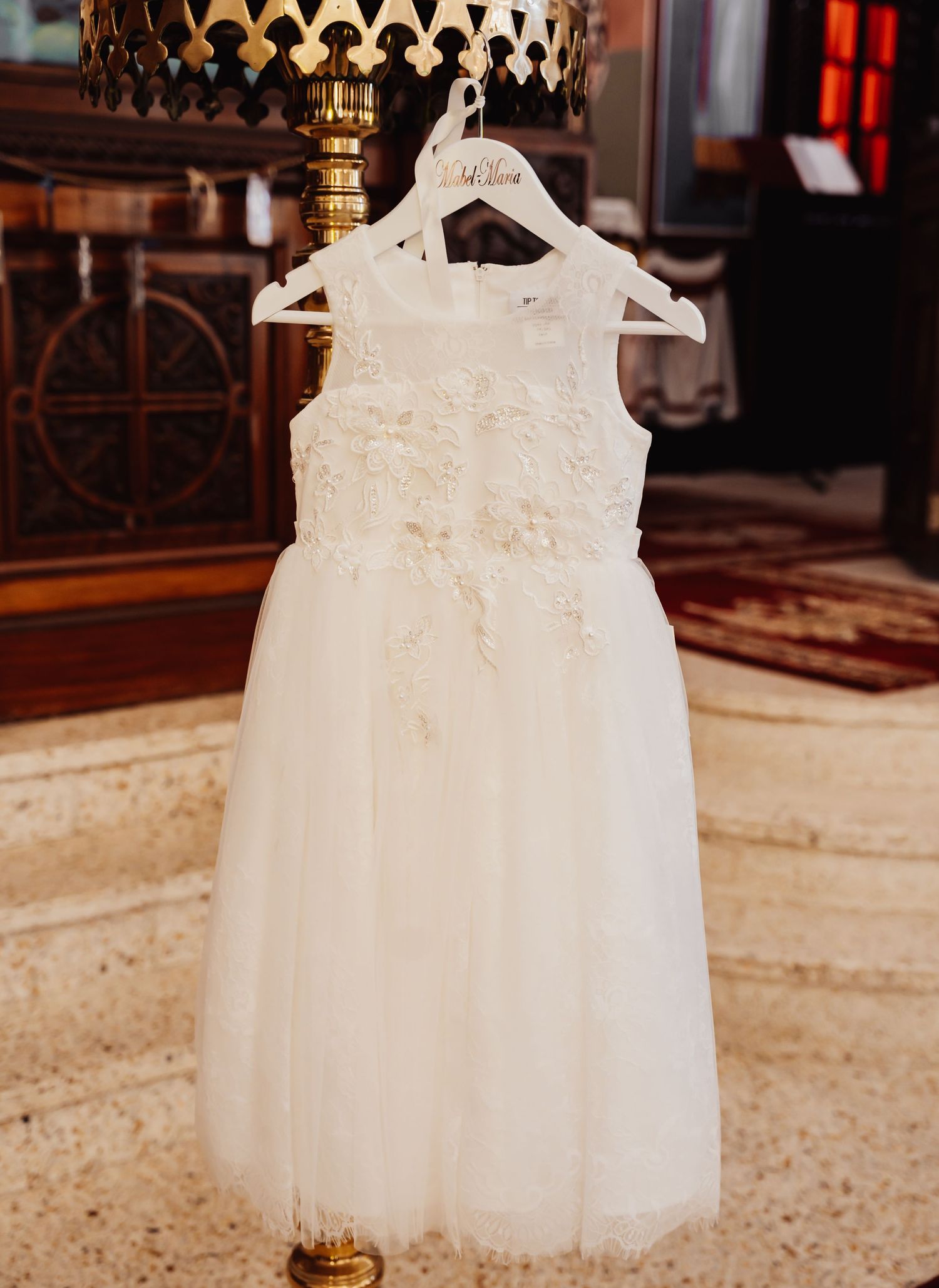 White tulle flower girl dress with delicate lace detailing hangs elegantly on display in an ornate church setting.