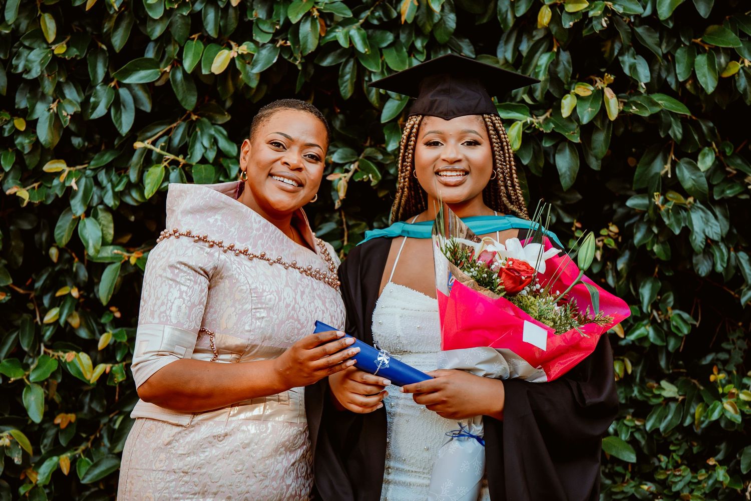 Two people share a joyful moment together while holding colorful gift bags against a leafy green background.