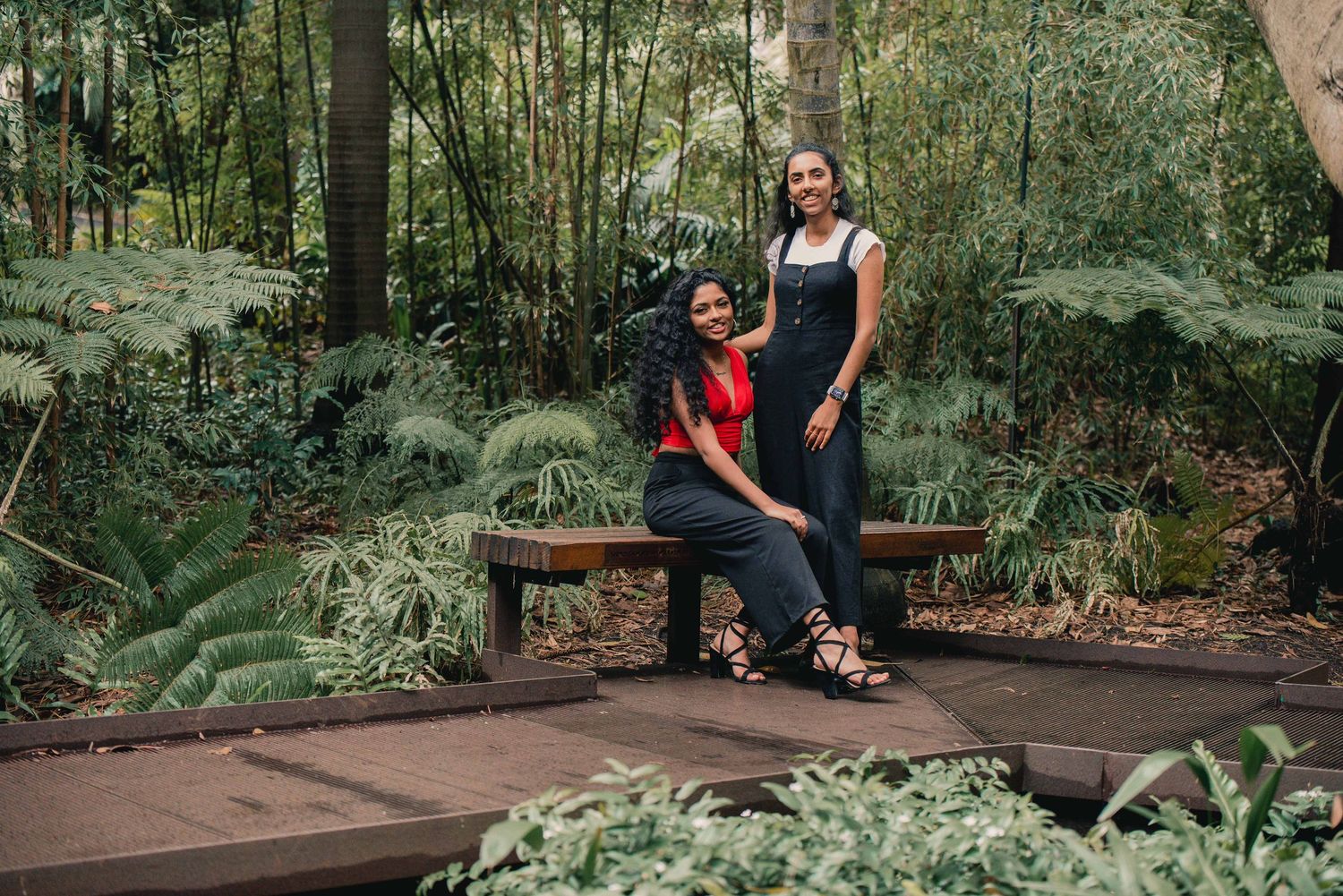 Wedding party gathers for photos on wooden boardwalk path surrounded by lush green forest vegetation.