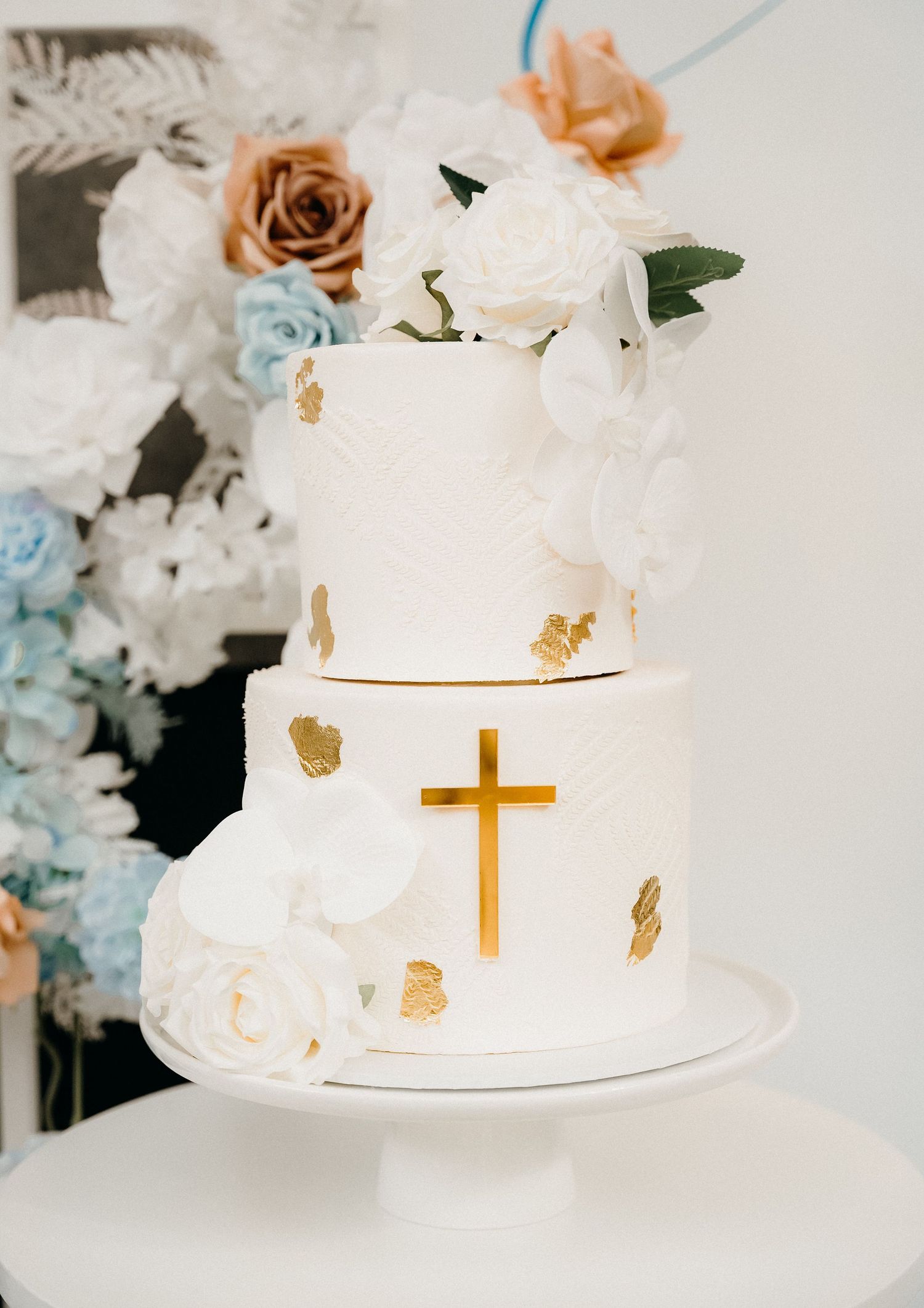 Elegant white wedding cake decorated with gold leaf accents and a delicate cross detail on multiple tiers.