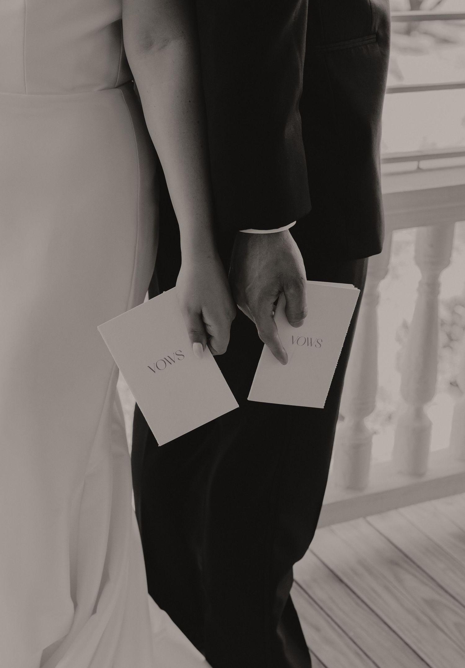 A black and white image of hands holding vow cards during a wedding ceremony.