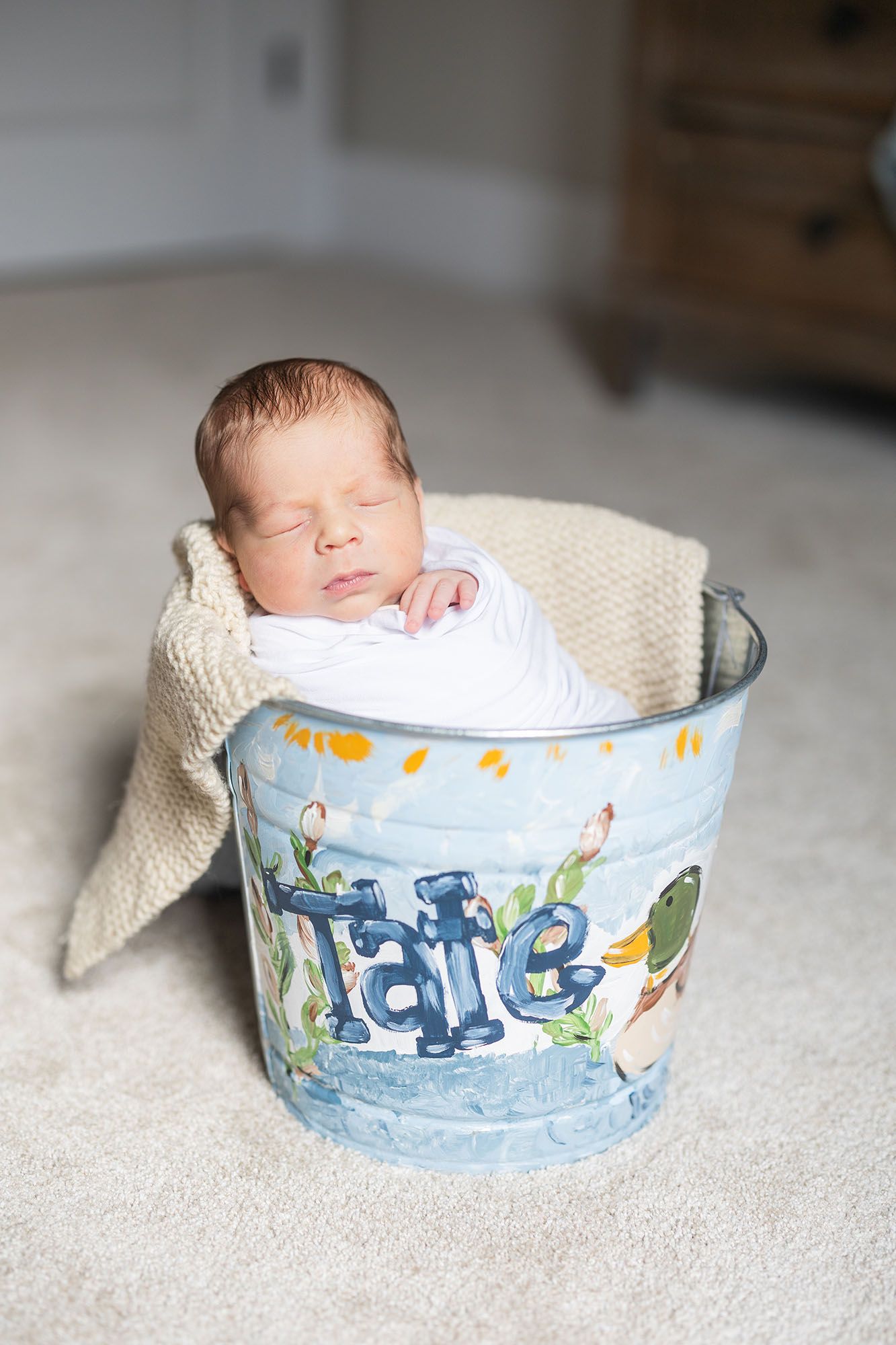 Baby swaddled and sitting up in a bucket that says 