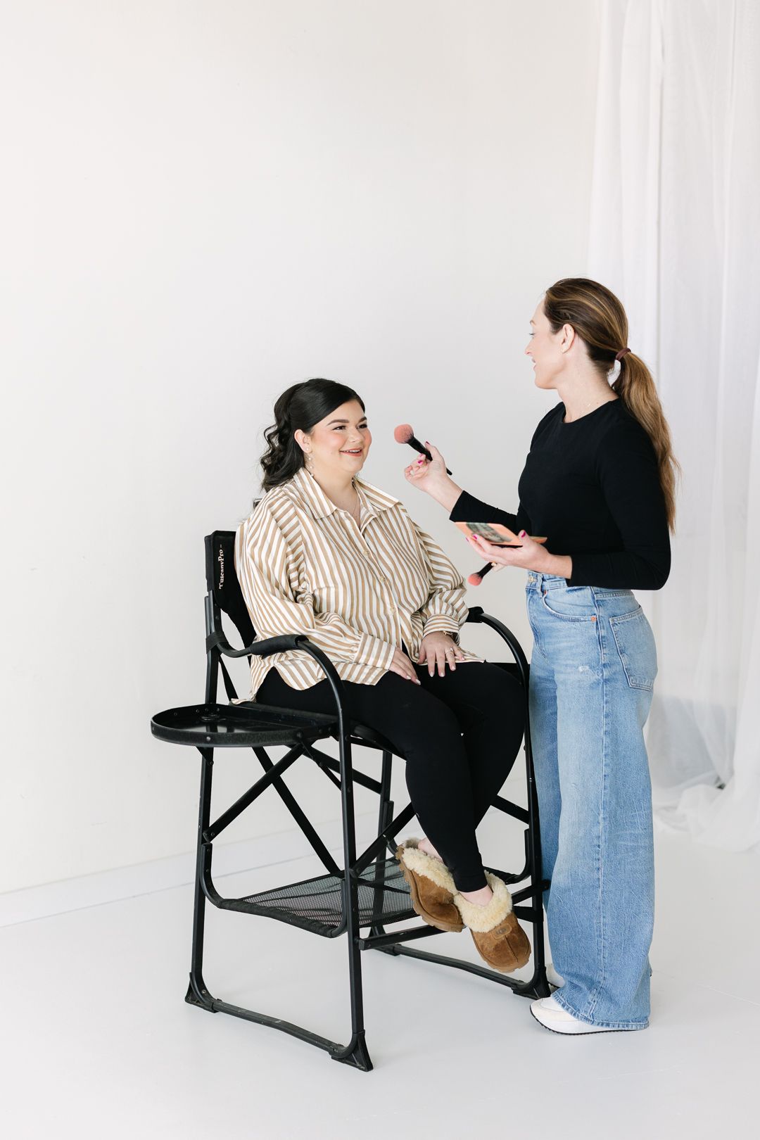 Mom sitting in a makeup chair getting makeup professionally done in all white studio.
