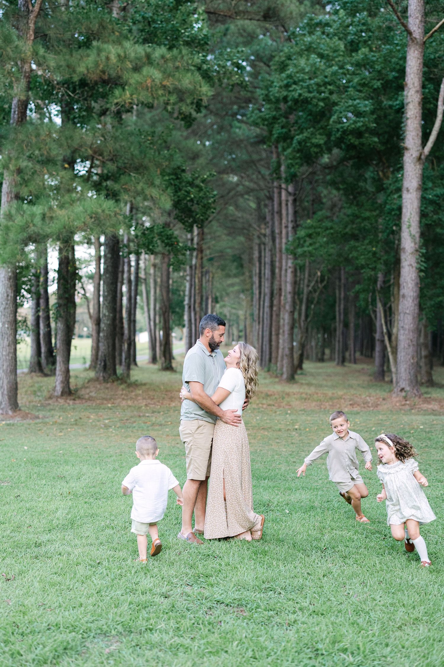 A family of five enjoying a family photography session in a field lined in pine trees.