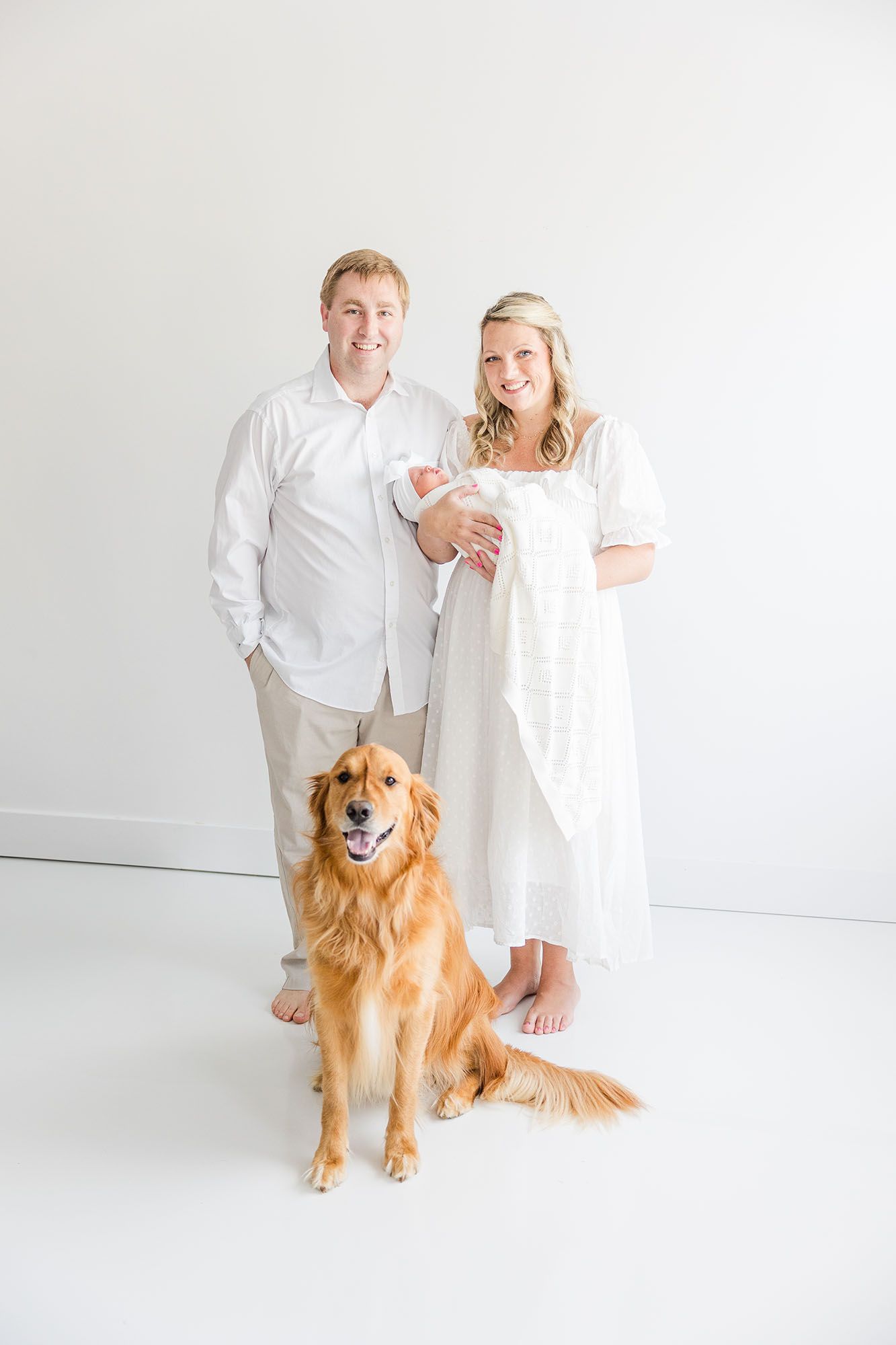 Mom, dad, baby, and golden retriever posing in an all white studio and in all white clothes.
