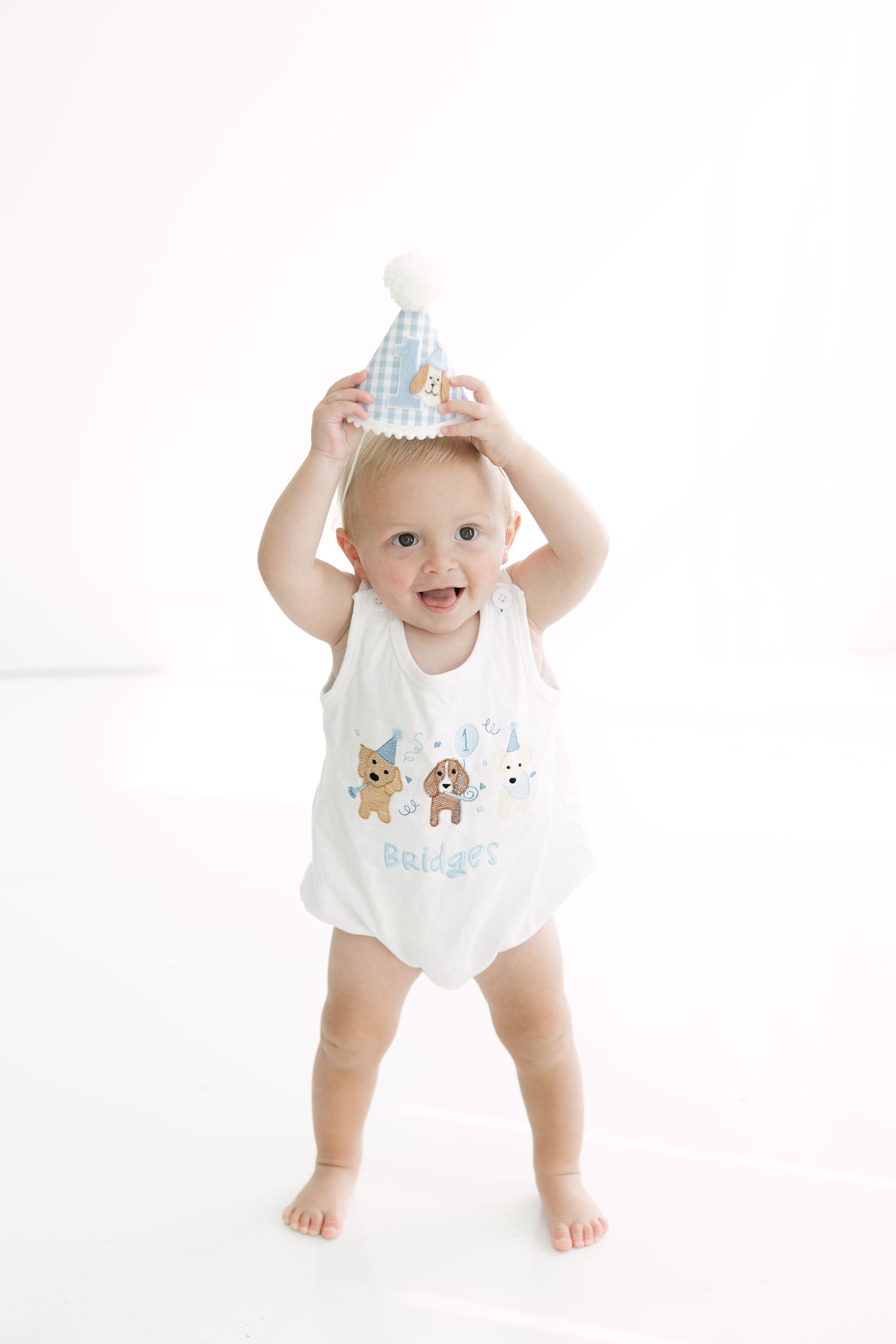 A happy baby wearing a white onesie with animal prints and designs against a white background by a Fairhope Photographer.