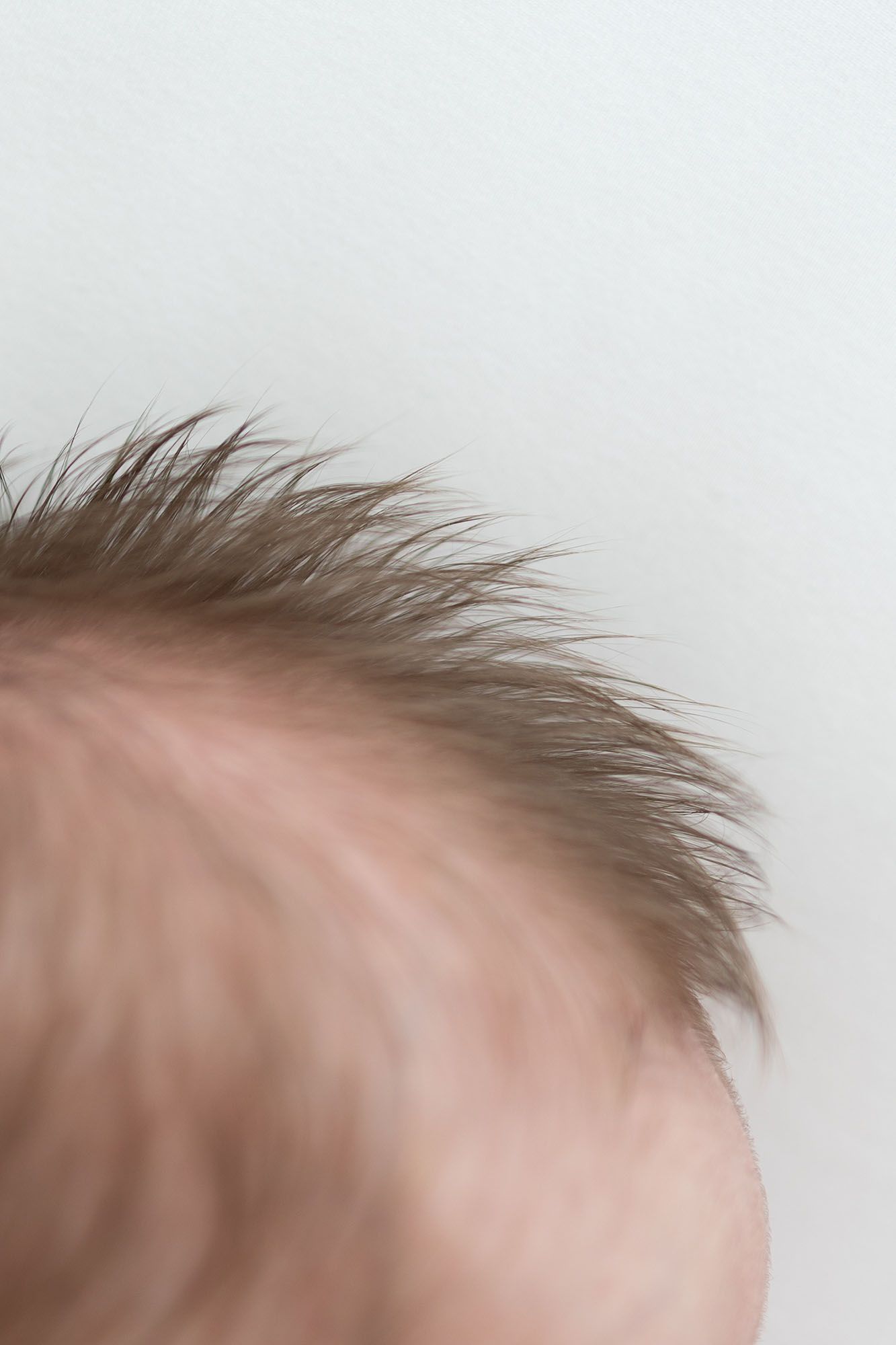 Close up image of baby's dark brown hair against a white sheet.