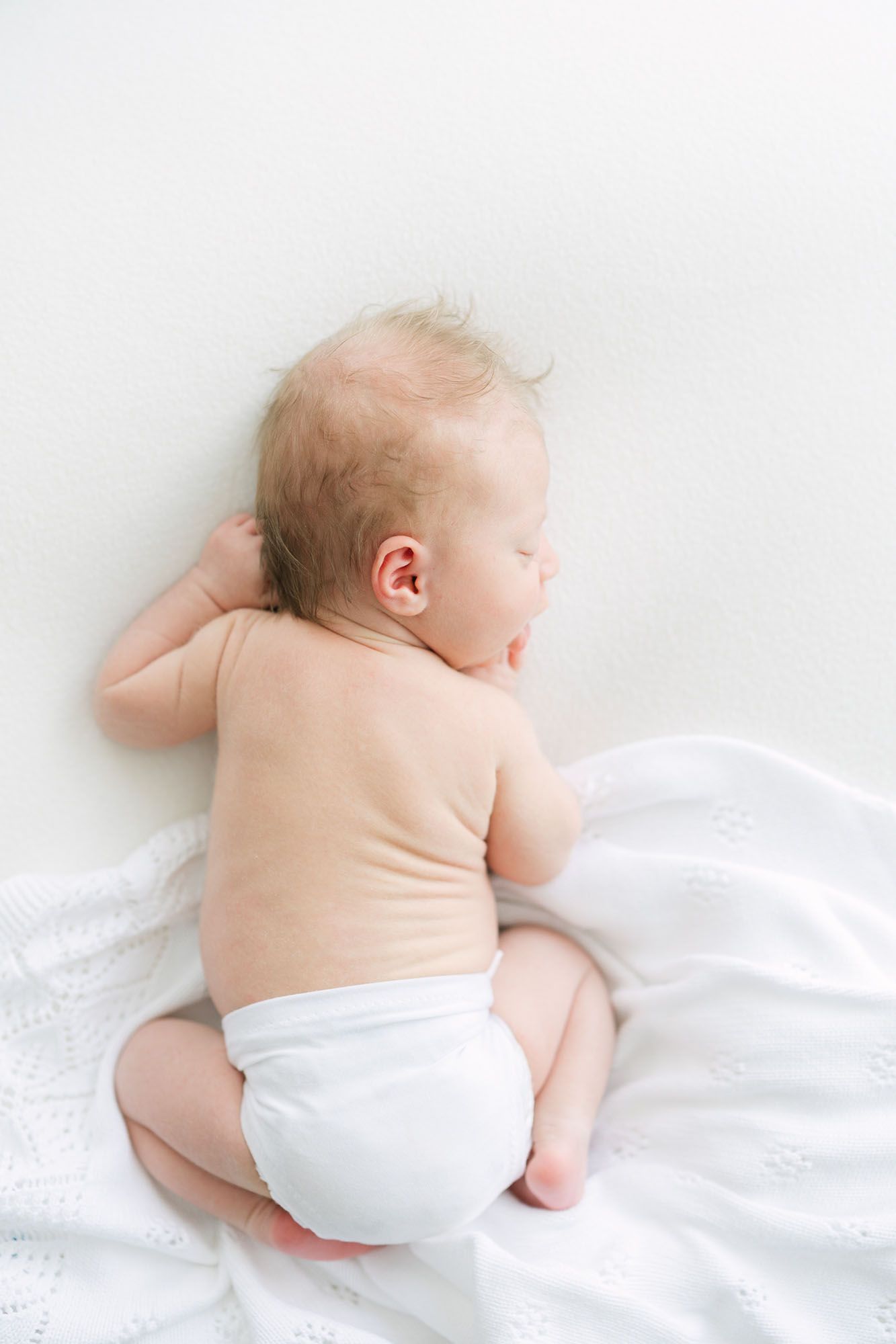 Baby laying on belly on white sheet scrunched to the side, captured by Mobile, AL Newborn Photographer, Alex Ishee.