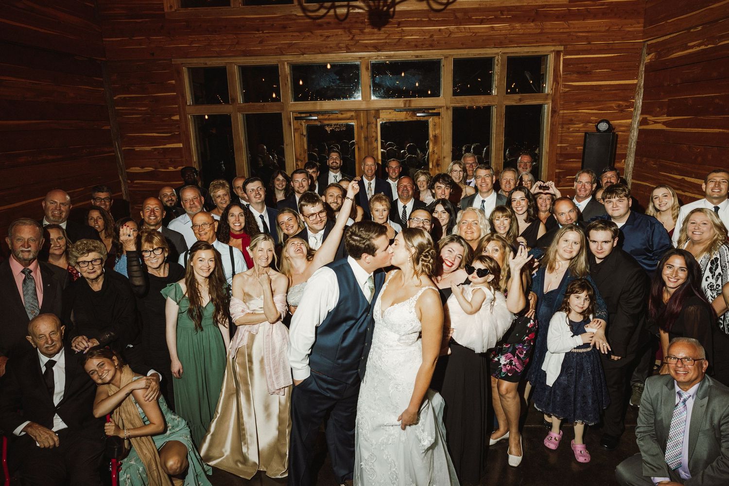 Wedding guests dance and celebrate together on a rustic wooden dance floor during an evening reception.