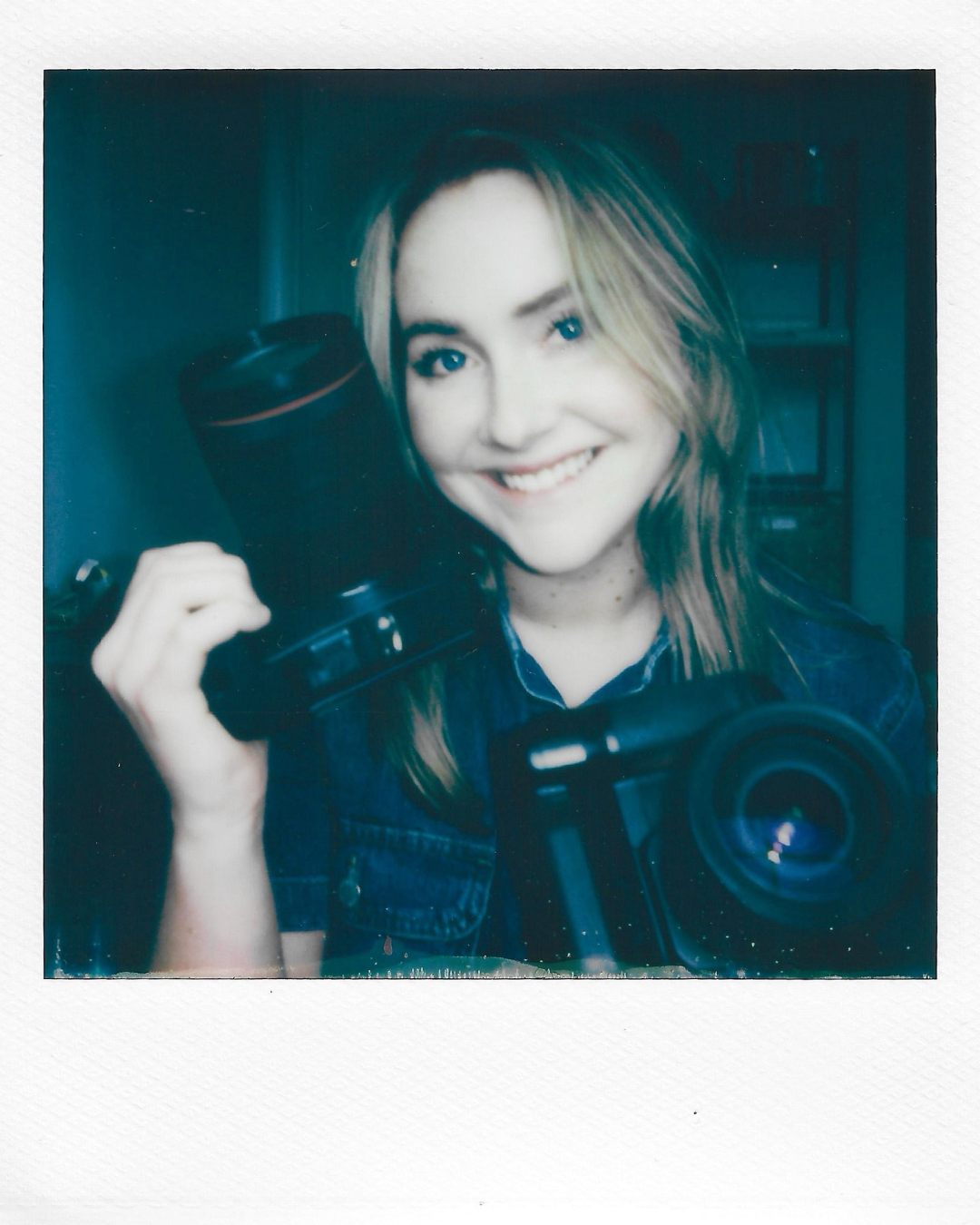 A photographer with blonde hair smiles at the camera while holding professional camera equipment in a polaroid-style photo.
