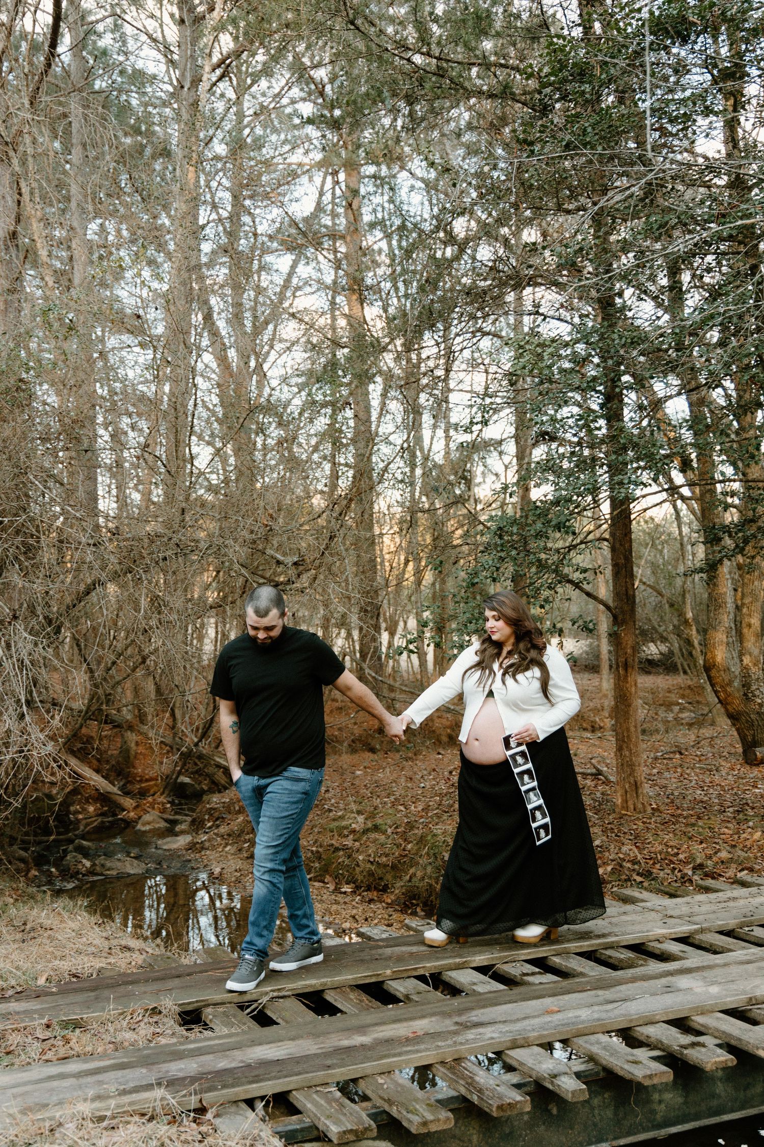 A couple walking hand in hand along old railroad tracks through a wooded forest area on an autumn day.