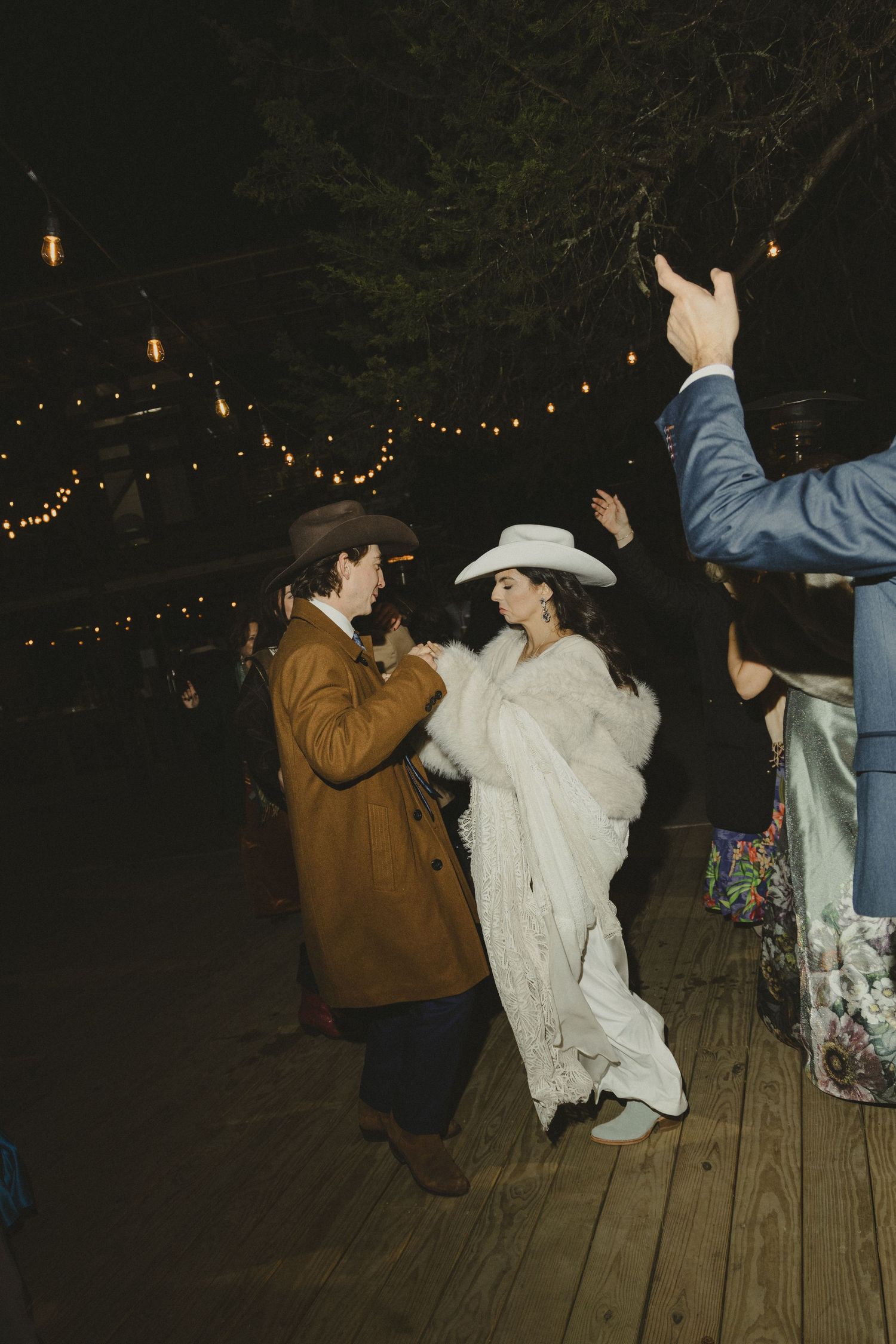 People dancing and celebrating under string lights at outdoor nighttime event.