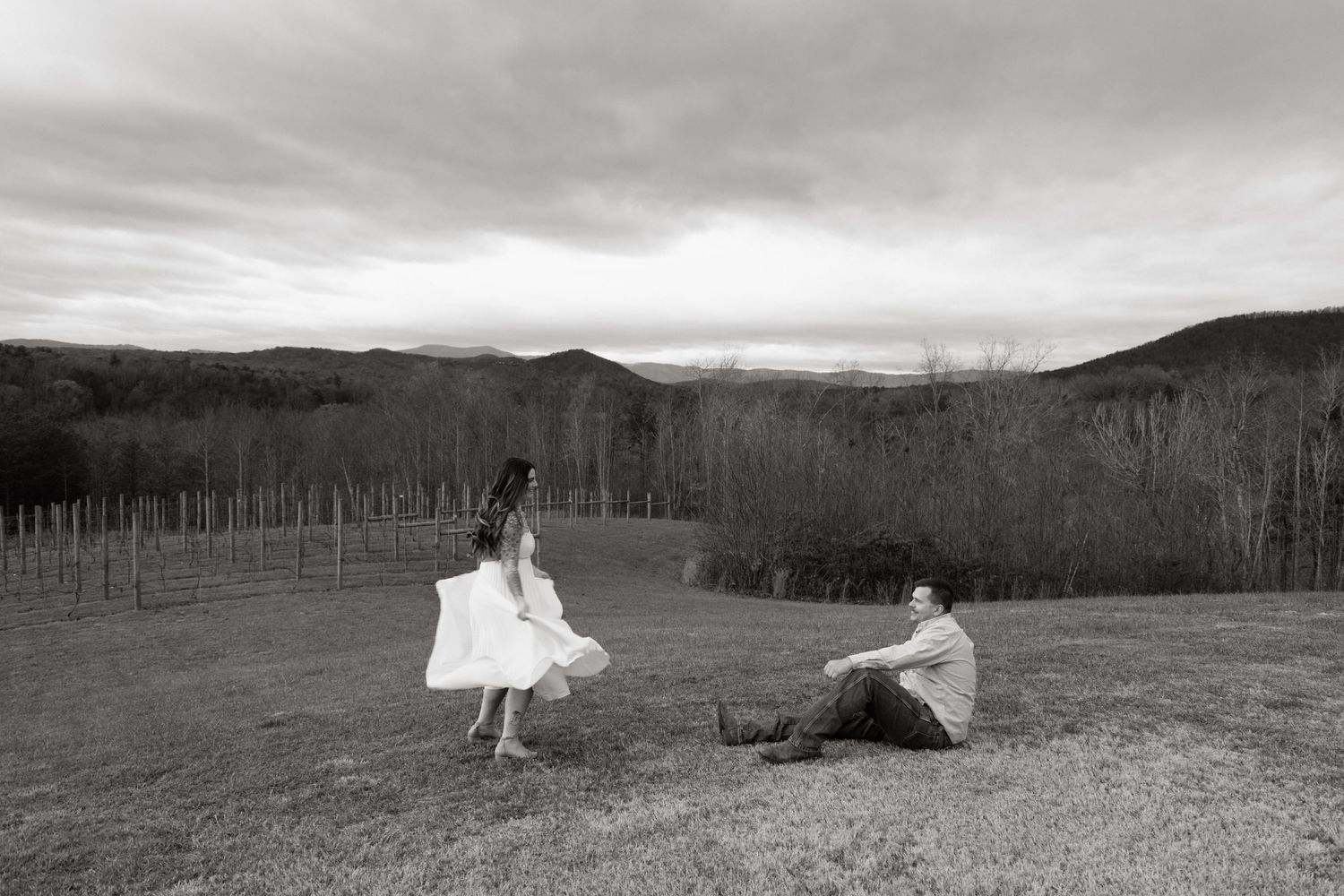 Black and white photo of couple in wedding attire posing playfully in mountain field.