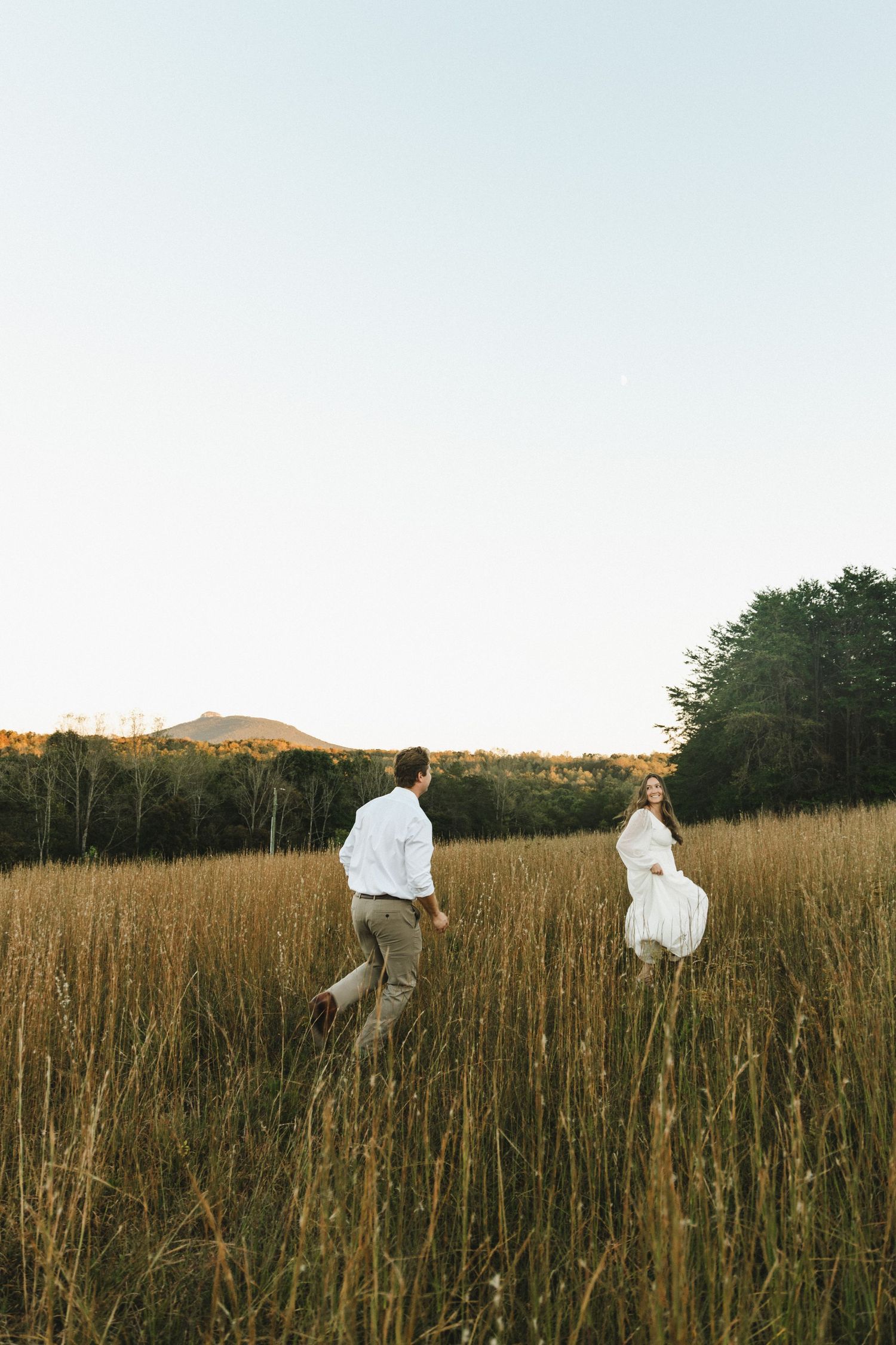 Two people running through a golden field at sunset with mountains in the distance.