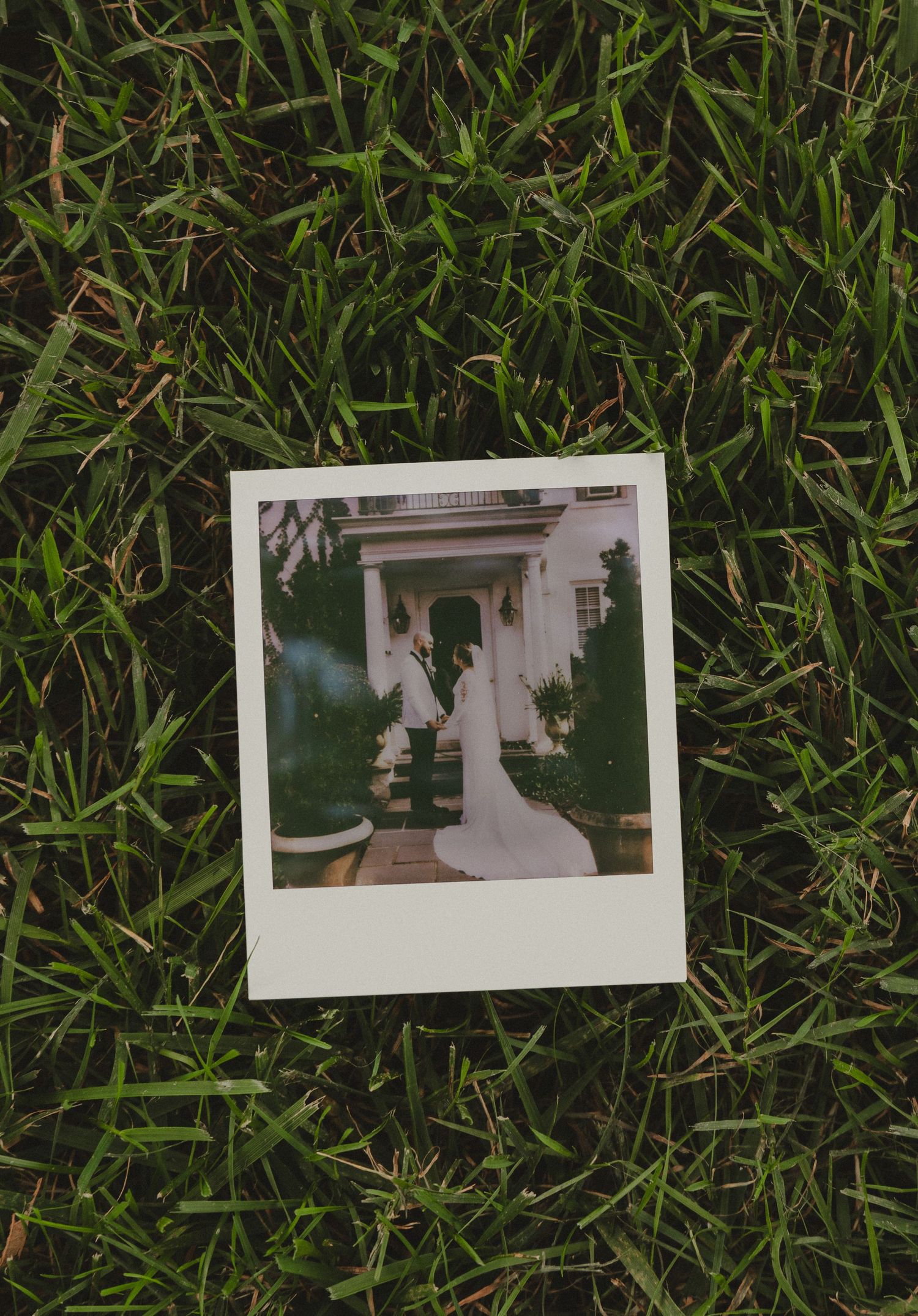 A Polaroid photo showing an elegant white columned entryway lies on green grass.