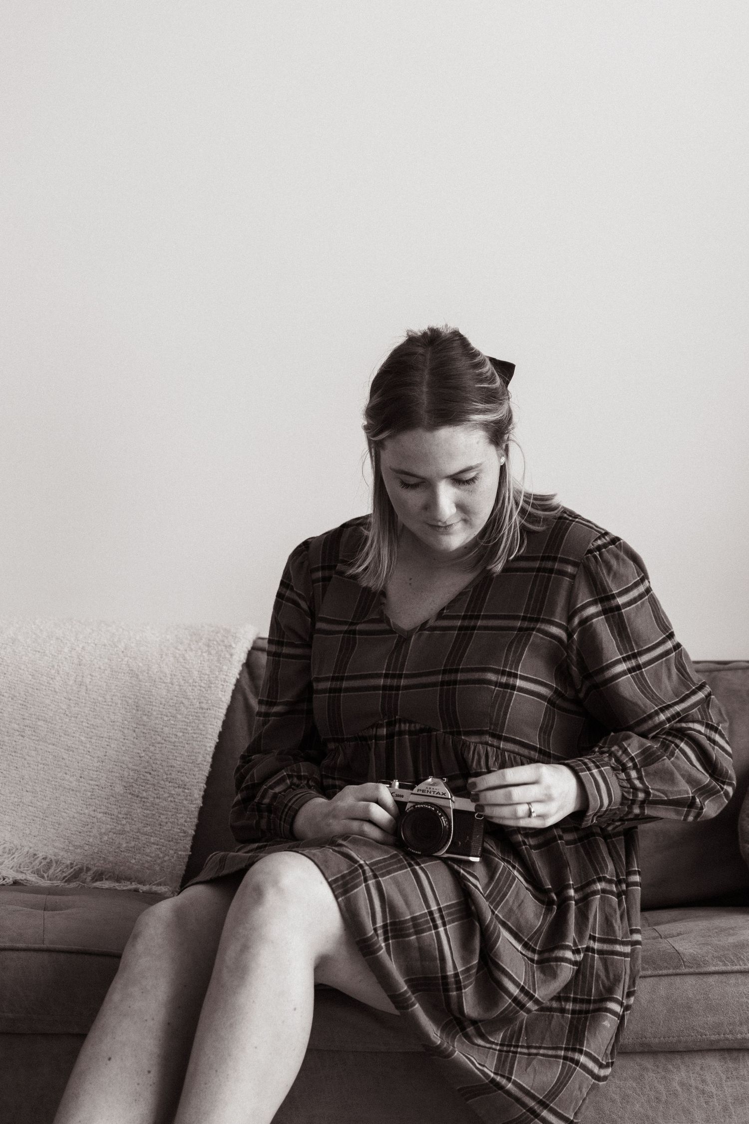 Monochrome photo of person in plaid dress looking down while holding camera on couch.