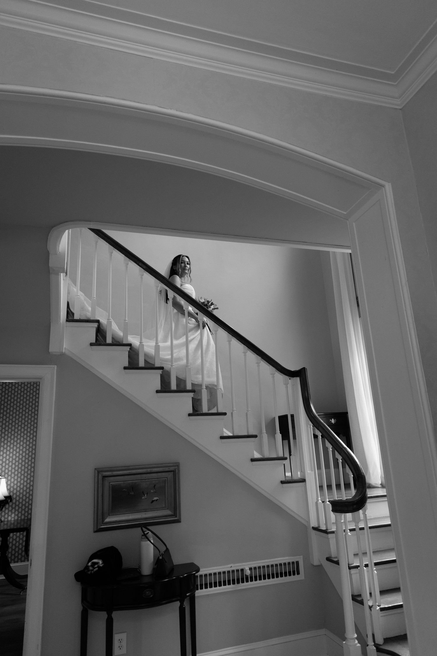 Elegant white staircase with dark wood handrails and steps curves gracefully upward in a traditional home interior.