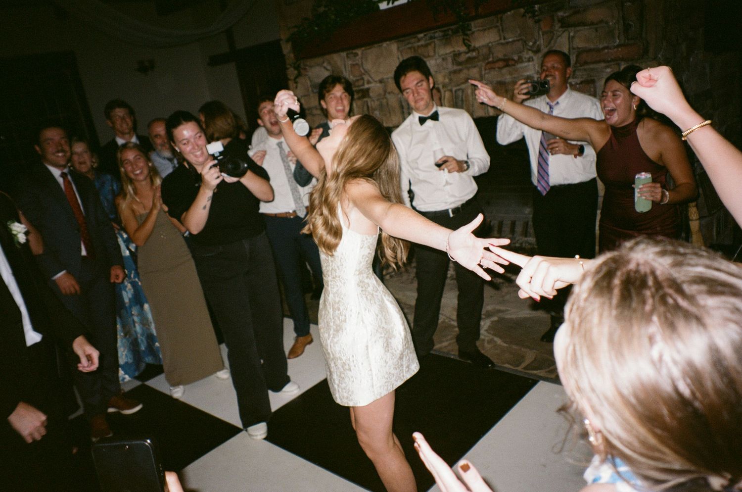 Wedding guests dance and celebrate on a dimly lit dance floor at a reception party.