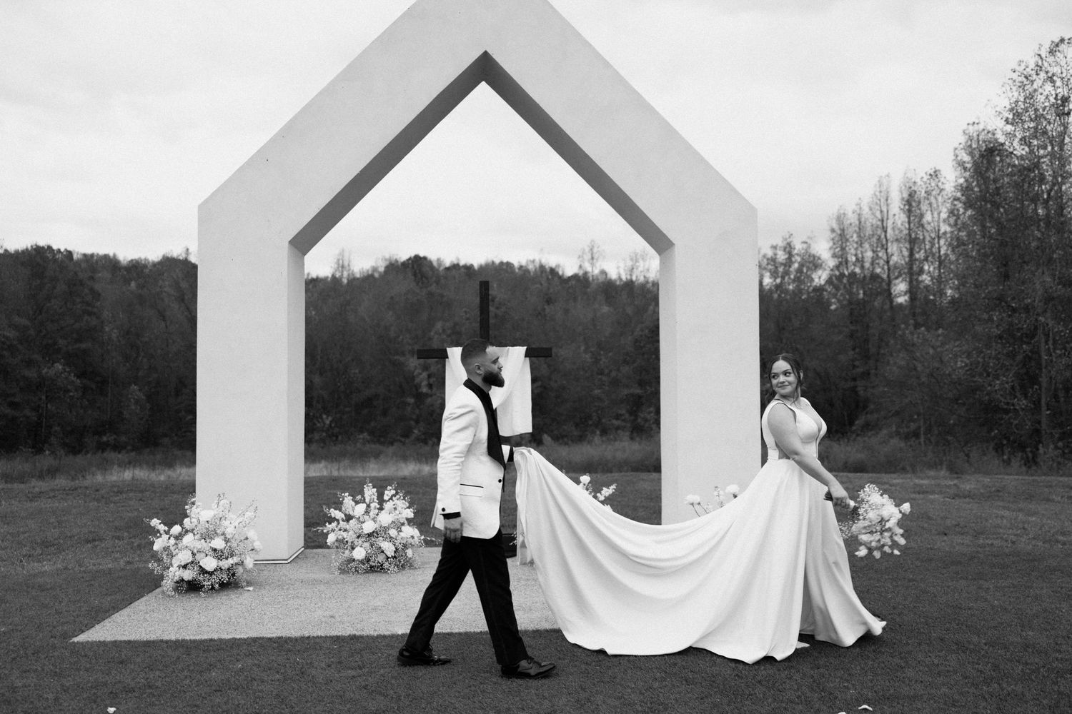 A black and white wedding photo series showing romantic poses of a couple in an outdoor setting with white architectural elements.