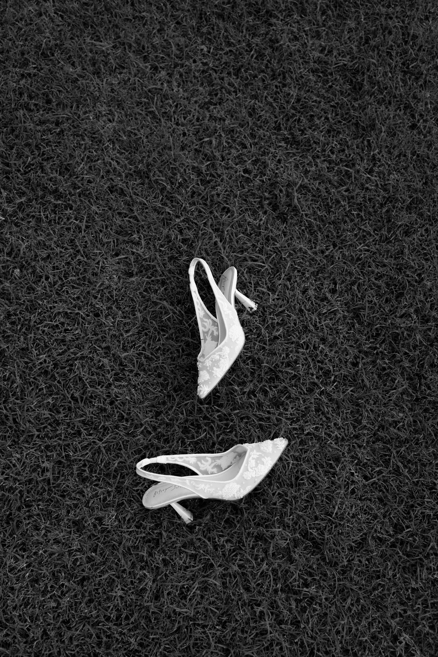 Four white high heel shoes displayed on a black textured background in a row.