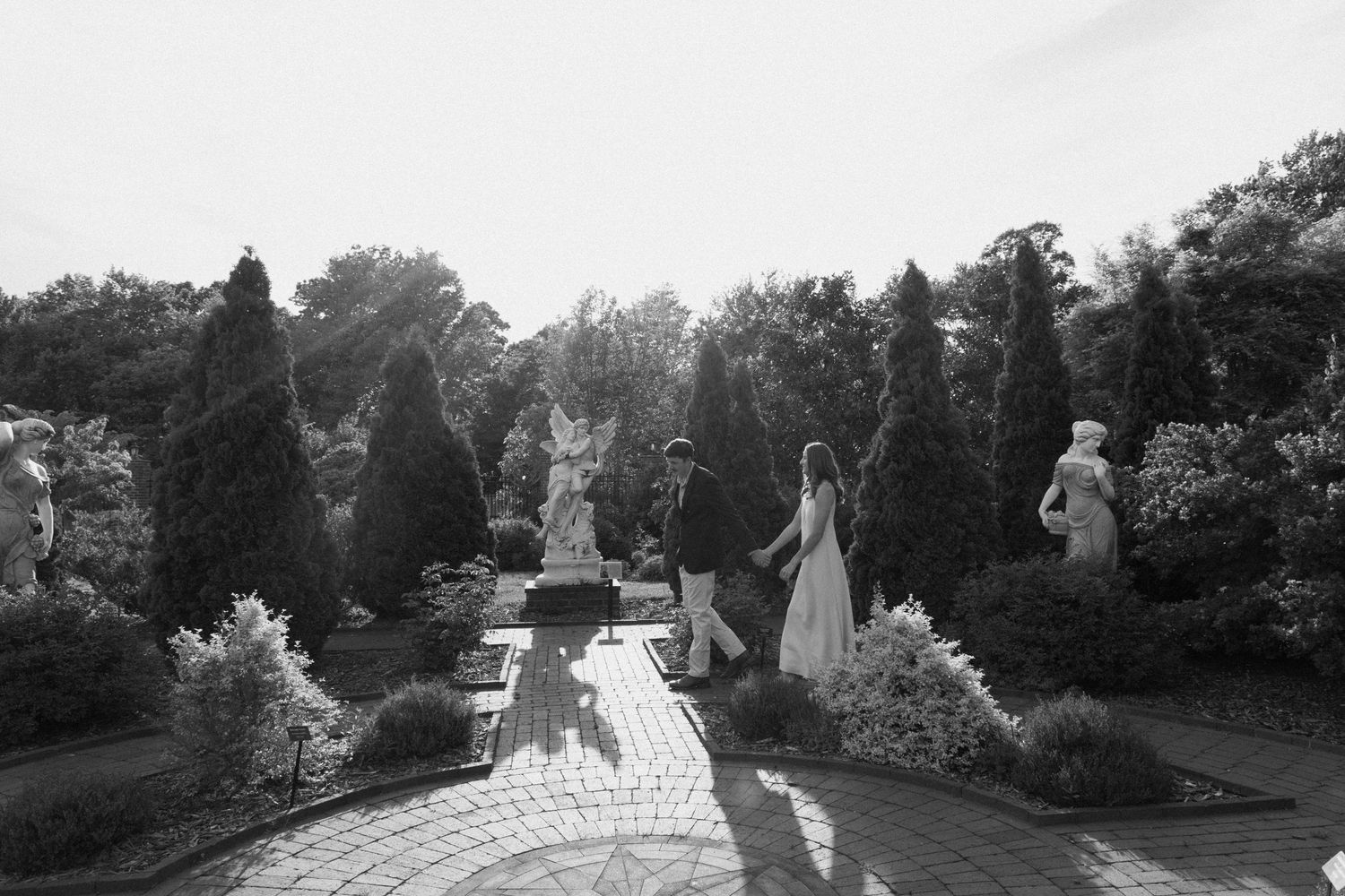 A scenic winding garden path leads through lush trees and landscaping in black and white photography.