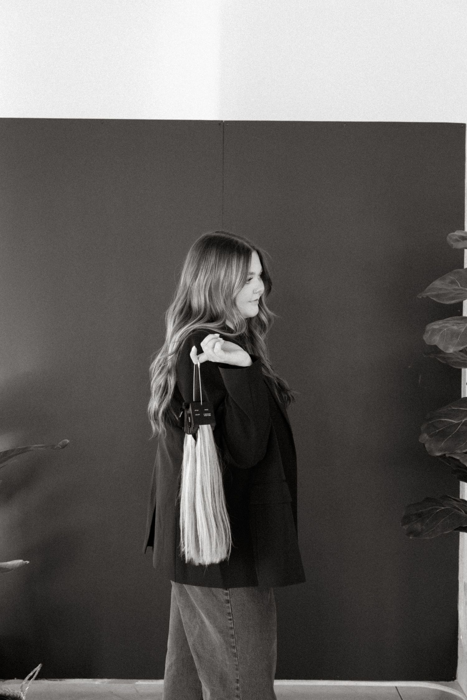 Black and white portrait of woman in dark blazer and jeans with long white tassel accessory, shown in profile.
