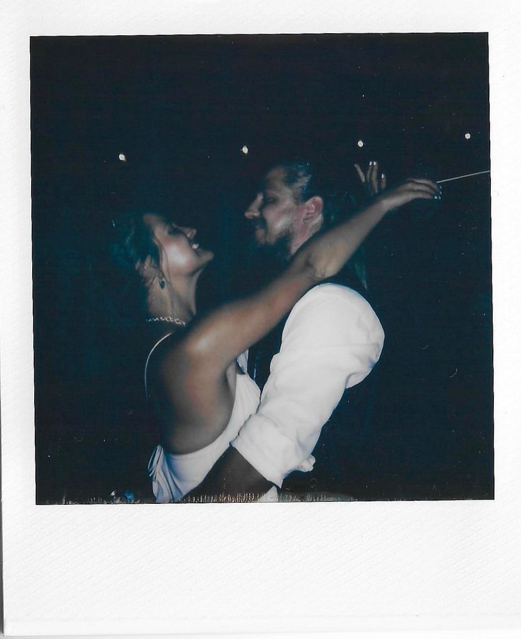 A couple shares a romantic dance moment in formal attire at an evening event, captured in a vintage polaroid style photo.