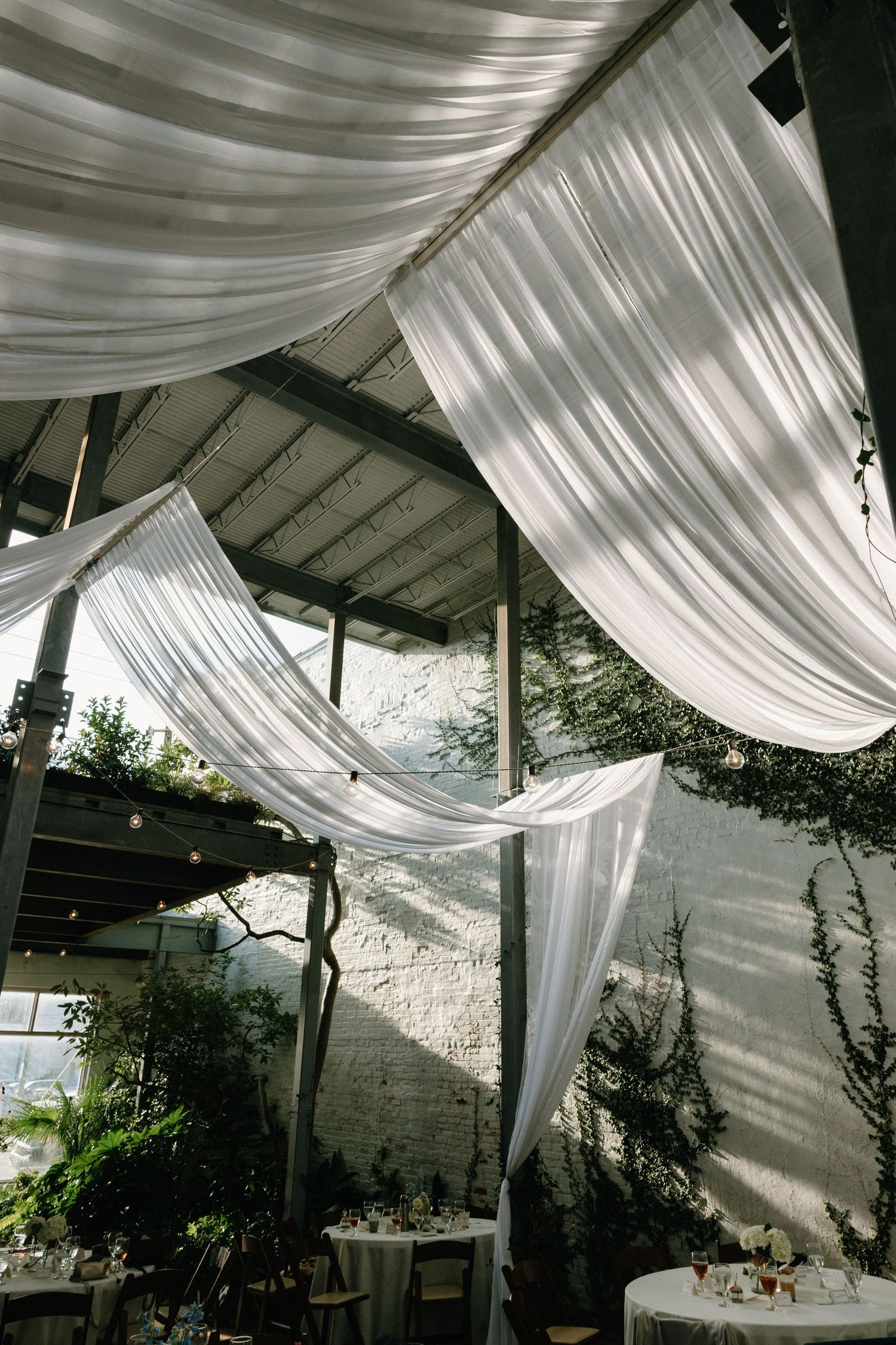 Elegant white fabric drapes create a romantic outdoor dining atmosphere with natural light filtering through the canopy.
