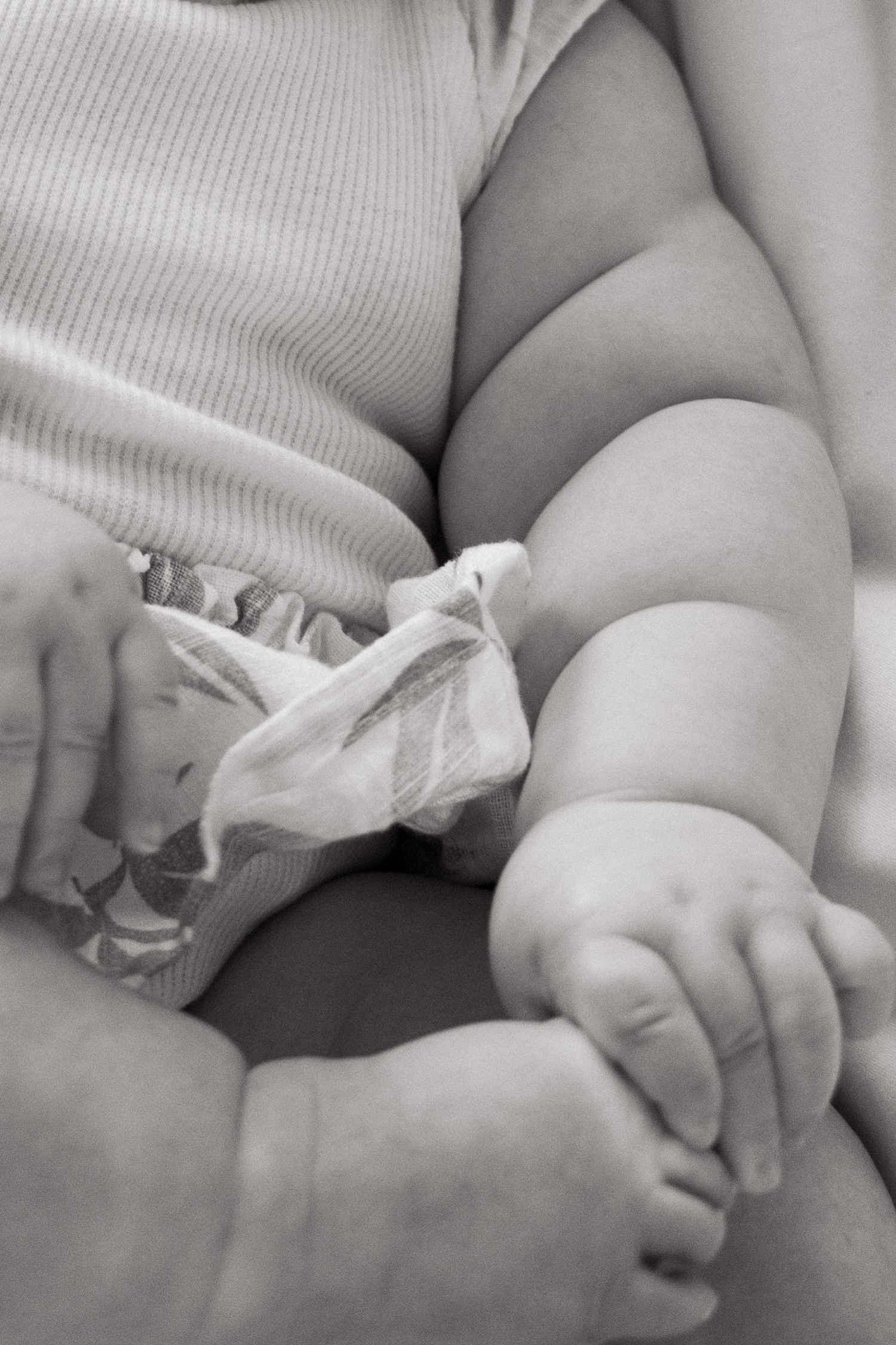 Close-up black and white photo of chubby baby legs, toes, and diaper in soft focus against a light background.