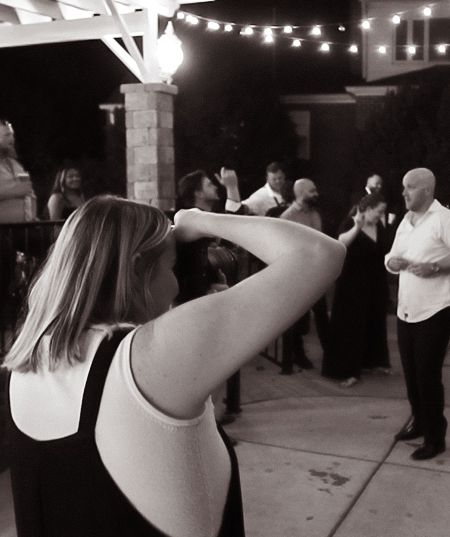 Black and white photo of photographer at work during evening outdoor event with string lights.