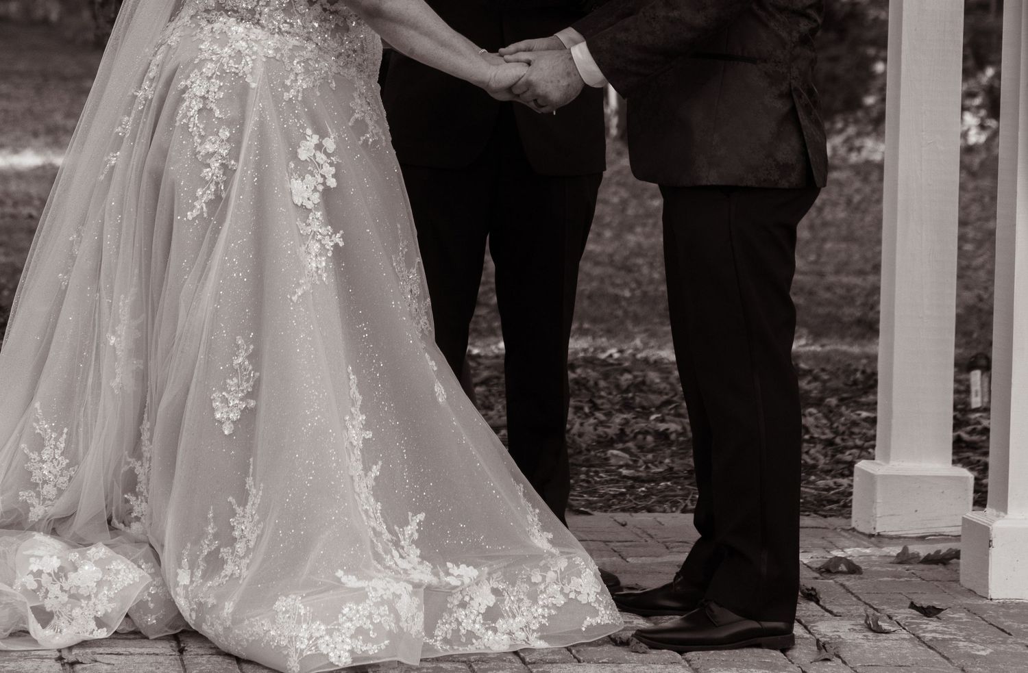 Black and white wedding ceremony detail showing bride's dress and groom's formal wear.