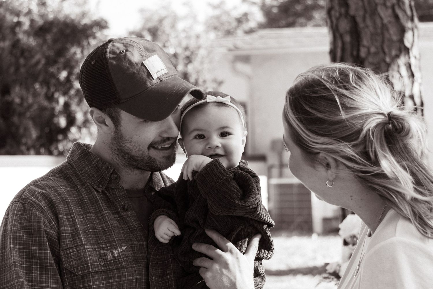 Black and white candid family moment captured outdoors on sunny day.