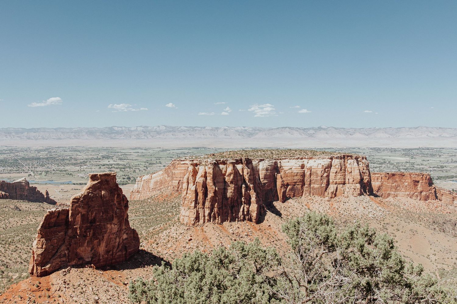 Dramatic red rock formations and cliffs in a desert landscape under blue sky.