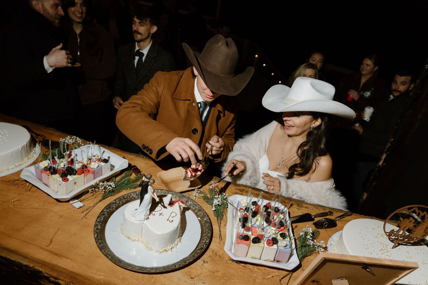 Hands cutting and serving slices of a round white frosted cake at a dinner party.