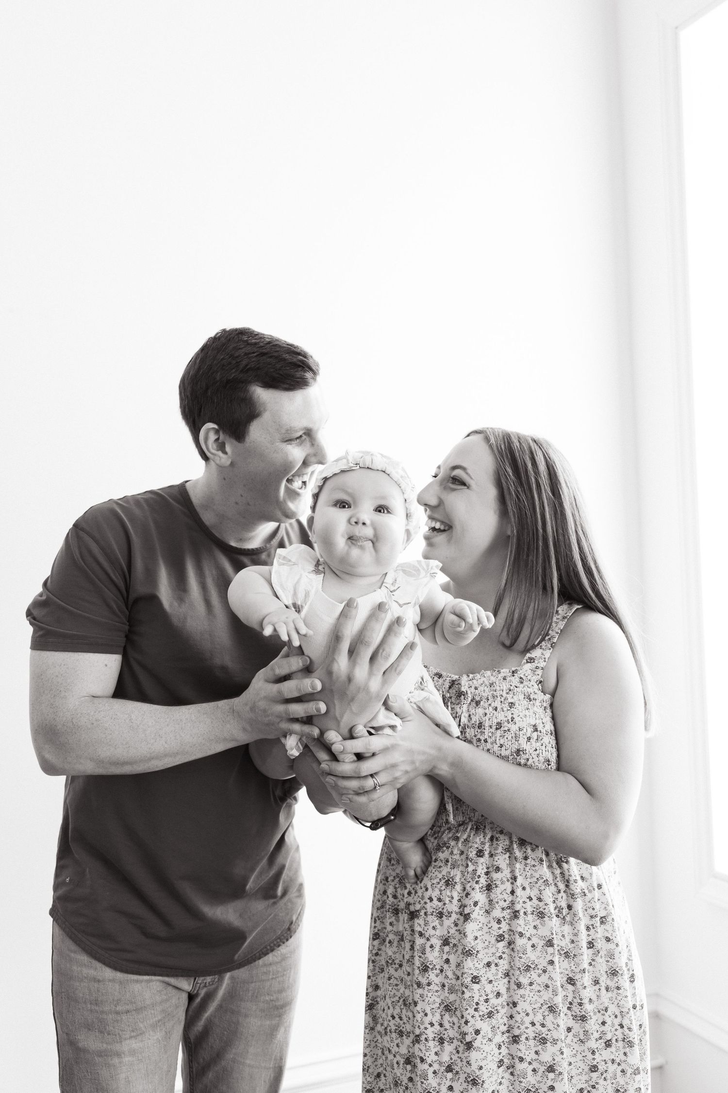 A joyful black and white family portrait showing parents holding and laughing with their baby against a white background.