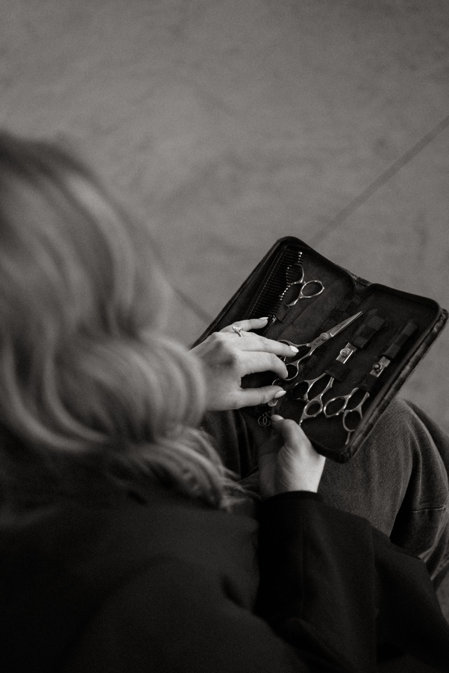 Black and white image of hands organizing hair styling tools in a professional kit.