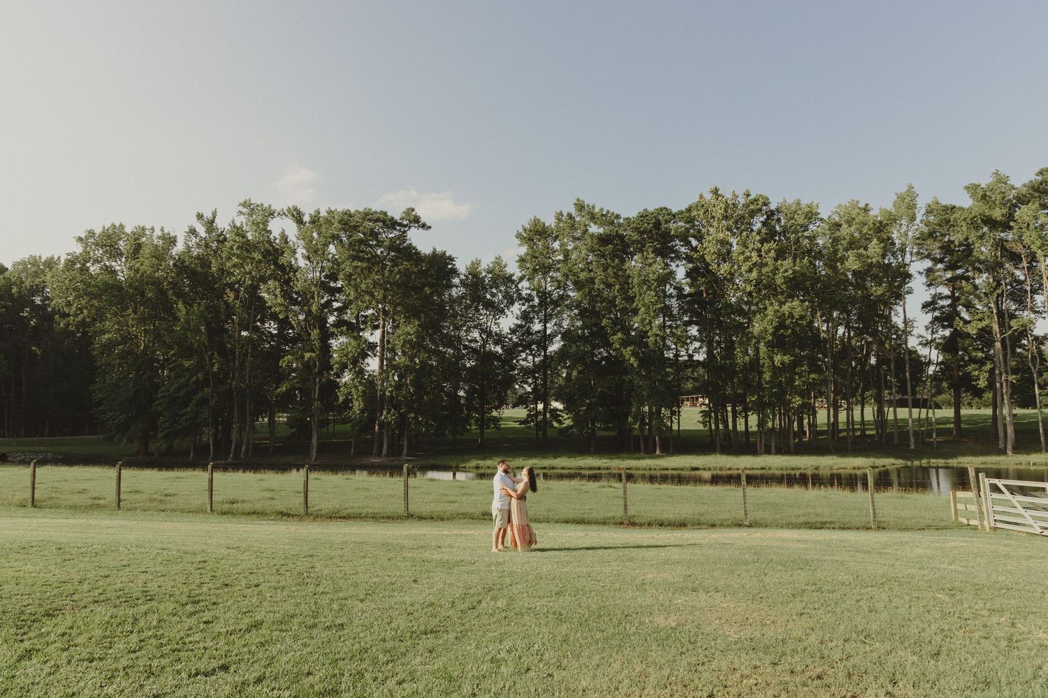 Panoramic view of a rolling green golf course with scattered trees and golfers in the distance on a sunny day.