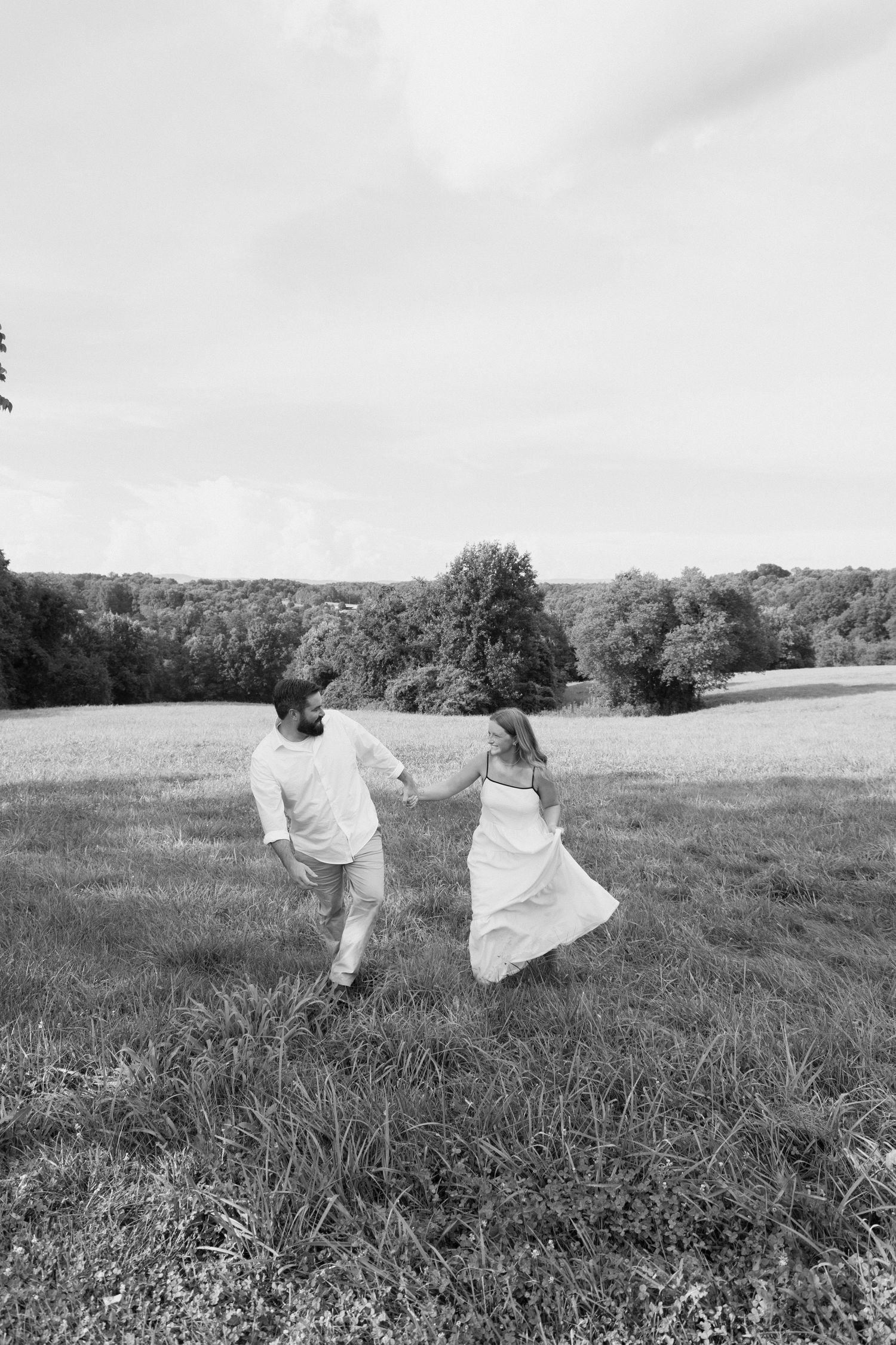 Black and white panoramic sequence shows a figure in white dress dancing gracefully across a grassy meadow landscape.