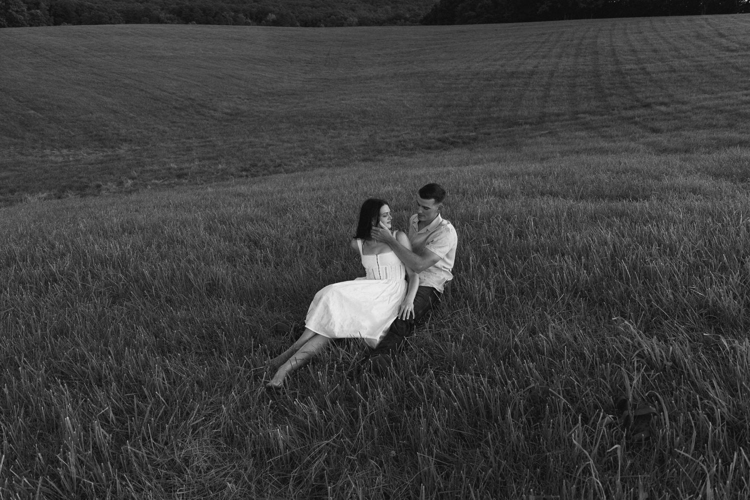 A couple lying together in a grassy field against a dramatic landscape backdrop.