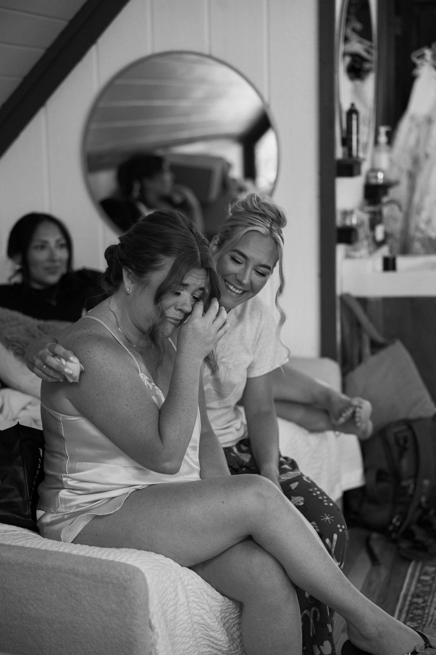 Black and white photo of two women sharing an emotional moment, laughing and embracing during wedding preparations.