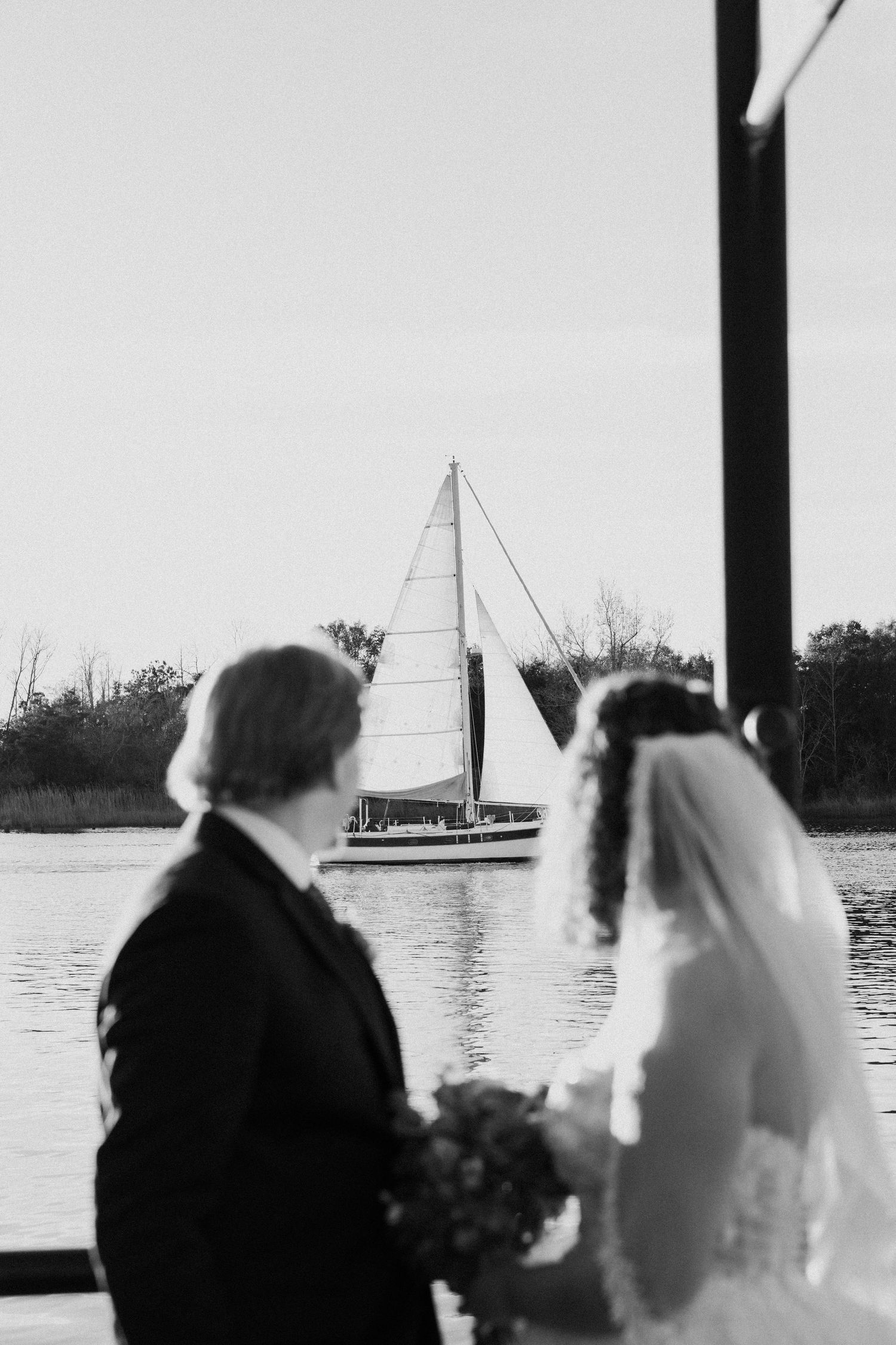 Black and white wedding photos show silhouettes of a couple by the water with sailboats in the background.