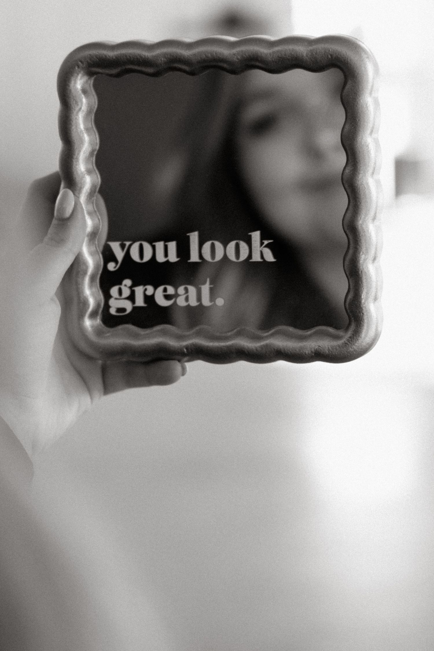 A blurred monochromatic image showing a mirror or frame with the text 'you look great' visible against a soft background.