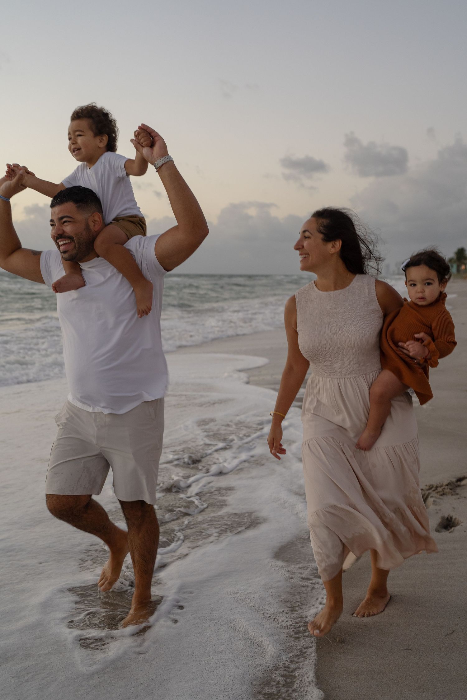 family at the beach - mom carrying 1 year old and dad giving 3 year old a piggyback