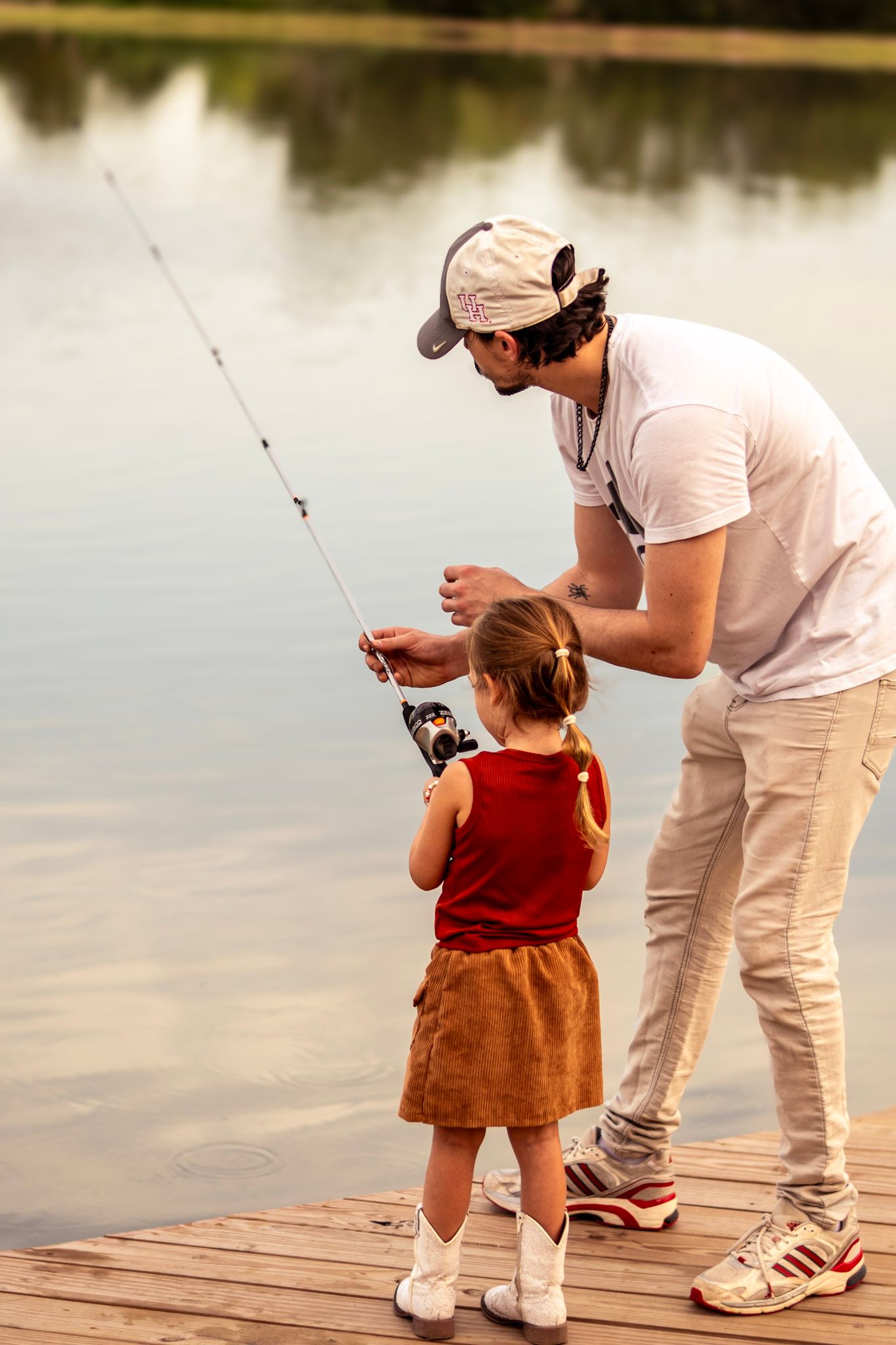 Candid moment of a dad laughing as his child reels in their first fish, with golden sunlight behind them.