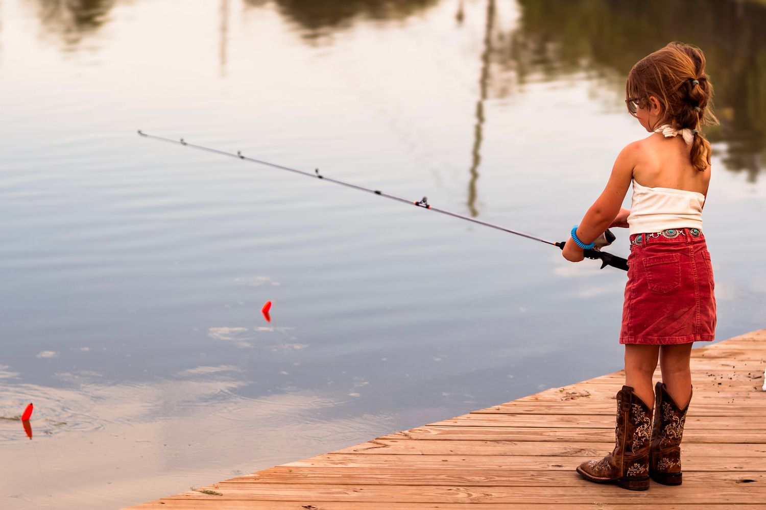 Peaceful lakeside scene with a family of four fishing, reflecting in the still sunset water.
