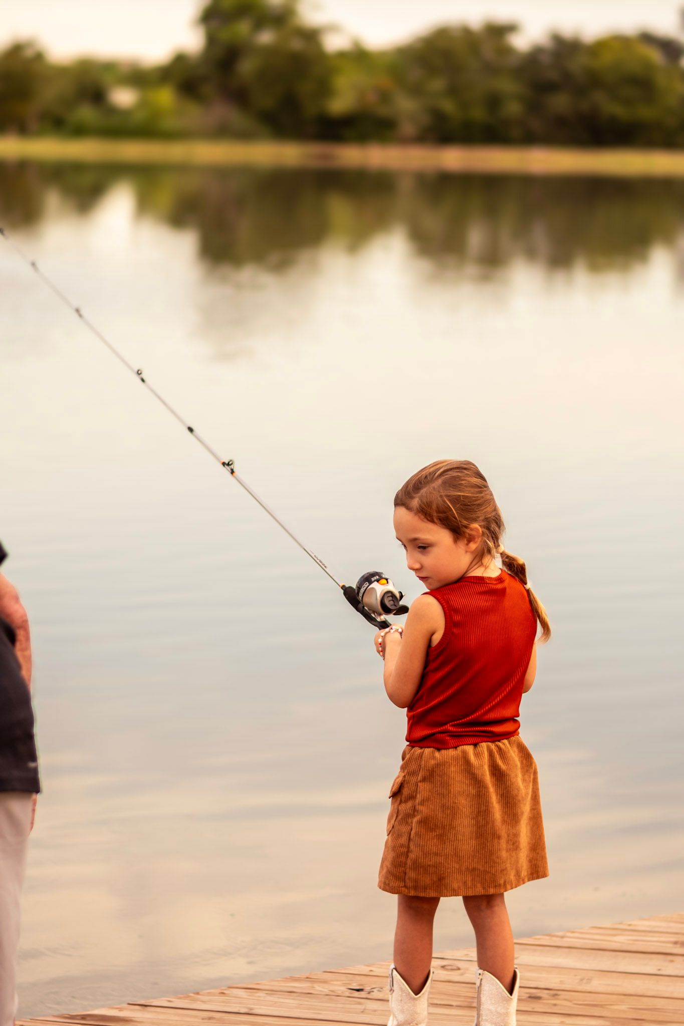 Candid photo of a child proudly holding a fishing rod, surrounded by the soft light of golden hour.