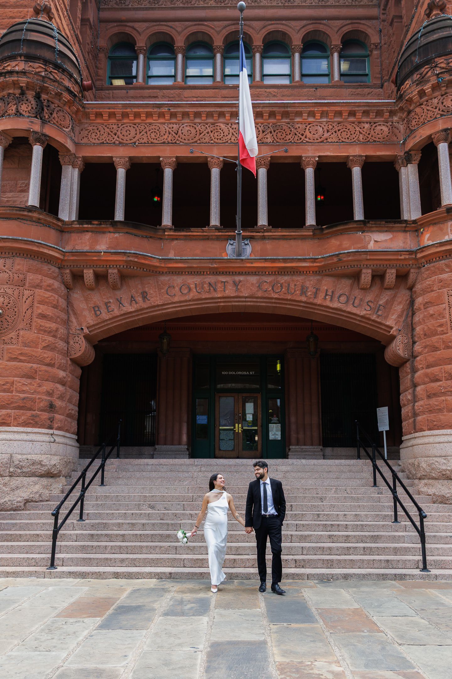 Bride and groom holding hands on steps of Bexar County Courthouse in San Antonio, Texas on their wedding day.